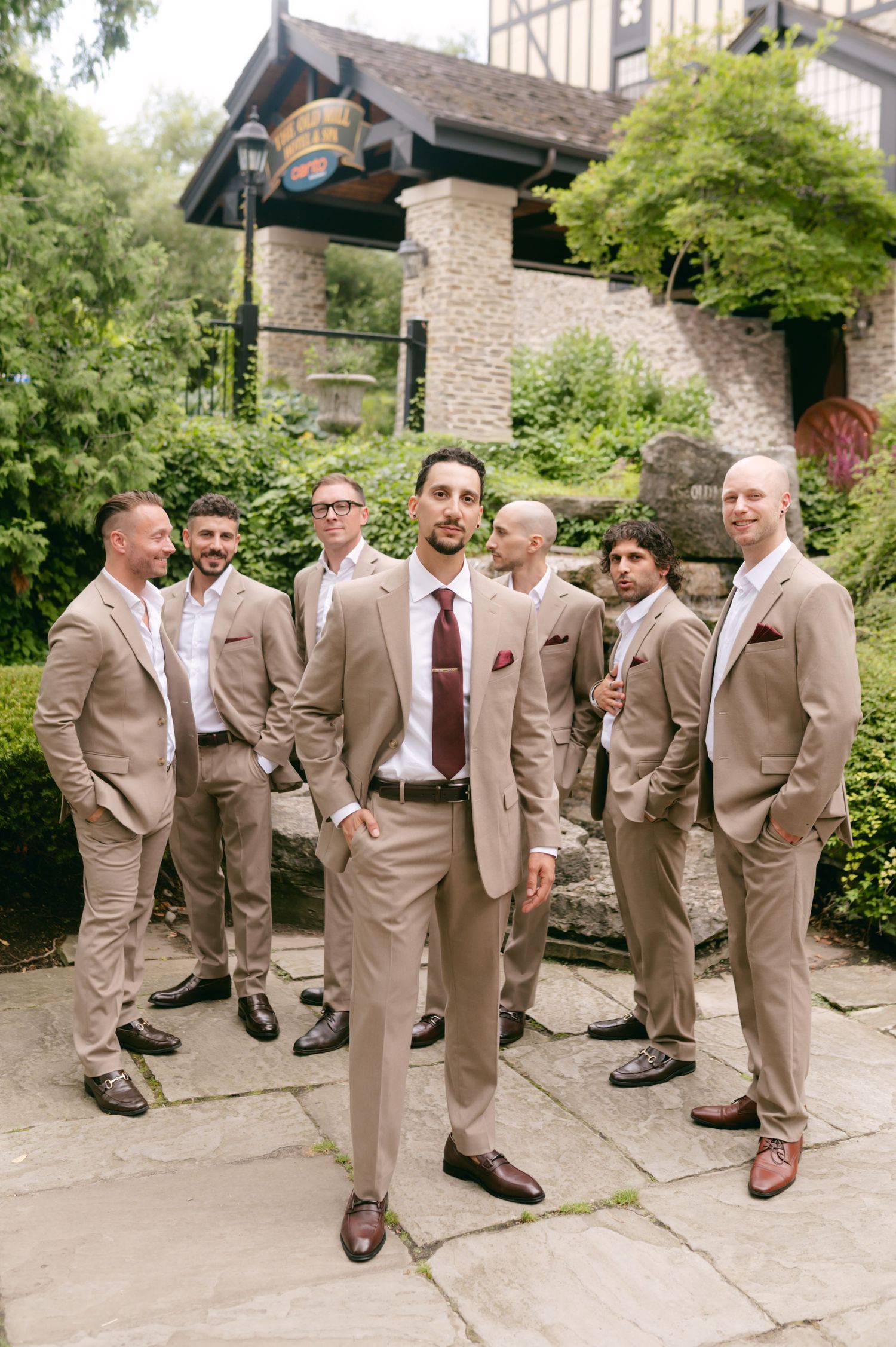 Groomsmen in tan suits and burgundy ties posing casually outdoors.