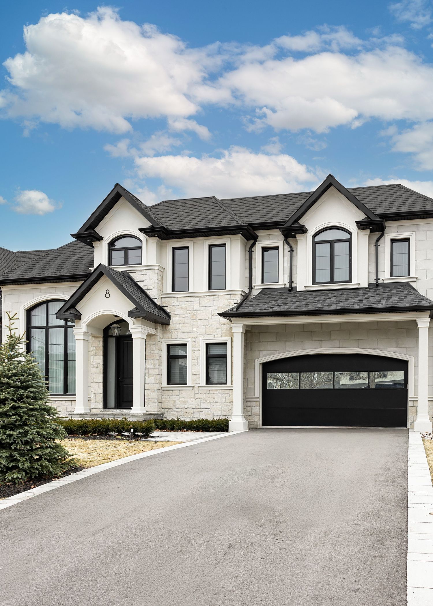 Contemporary house facade with black garage doors and white stone exterior viewed from driveway.