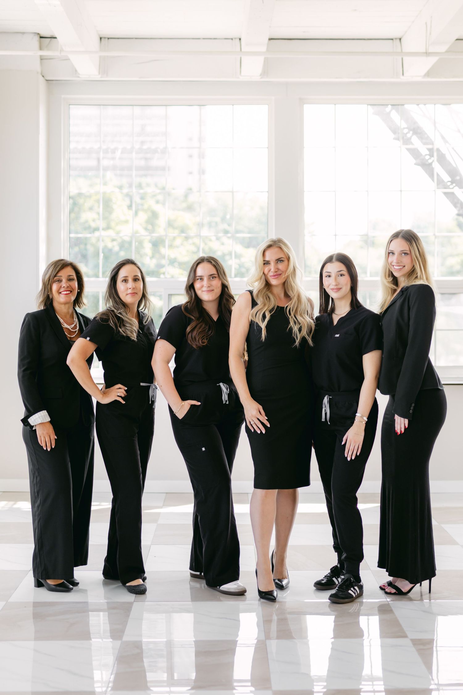 Group photo of women in black outfits posing creatively in bright white studio space.
