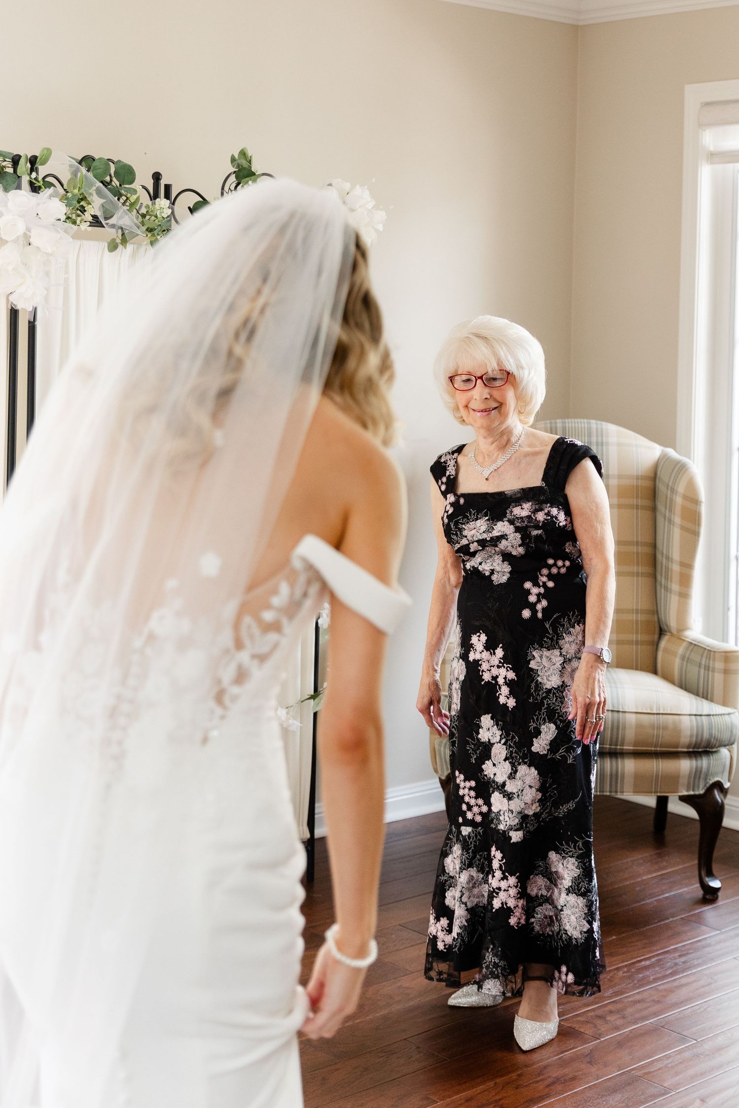 A bride in a white wedding dress shares an emotional first look moment with someone wearing a floral black dress.