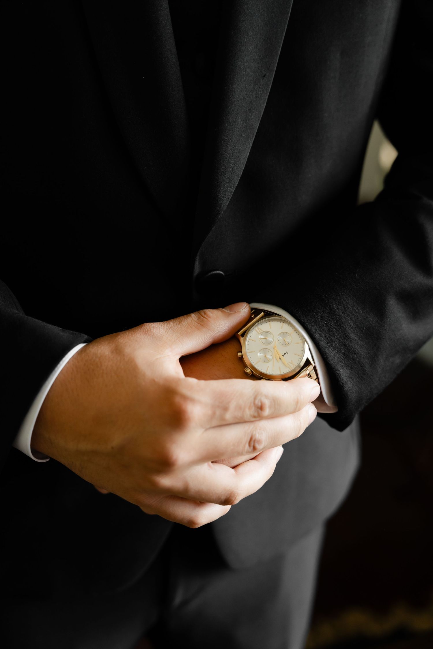 Close-up shots of hands adjusting a watch and cufflinks while wearing a black formal suit.