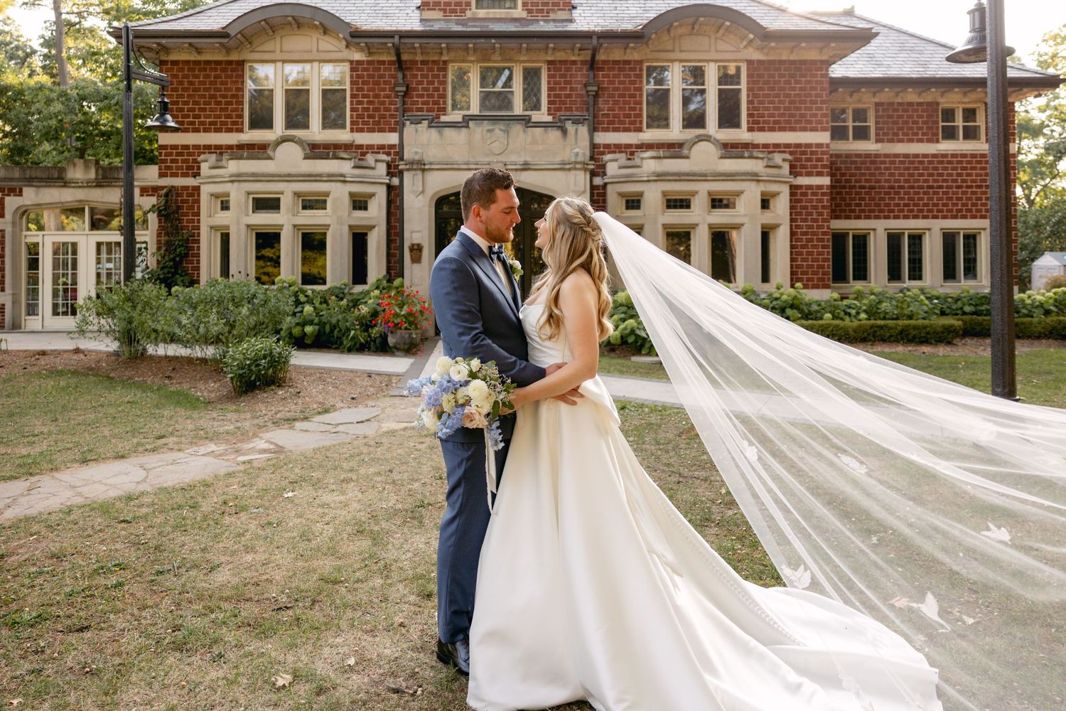 A romantic wedding couple dances together on a brick patio surrounded by elegant architecture.