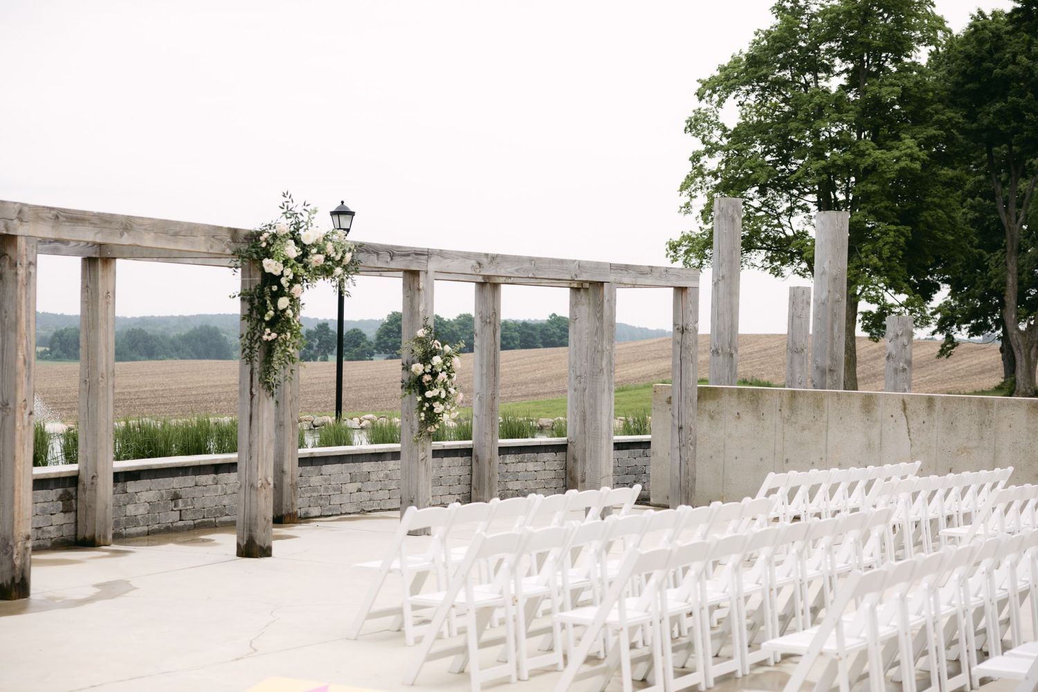 Outdoor wedding ceremony setup with white chairs and floral-decorated wooden pergola.