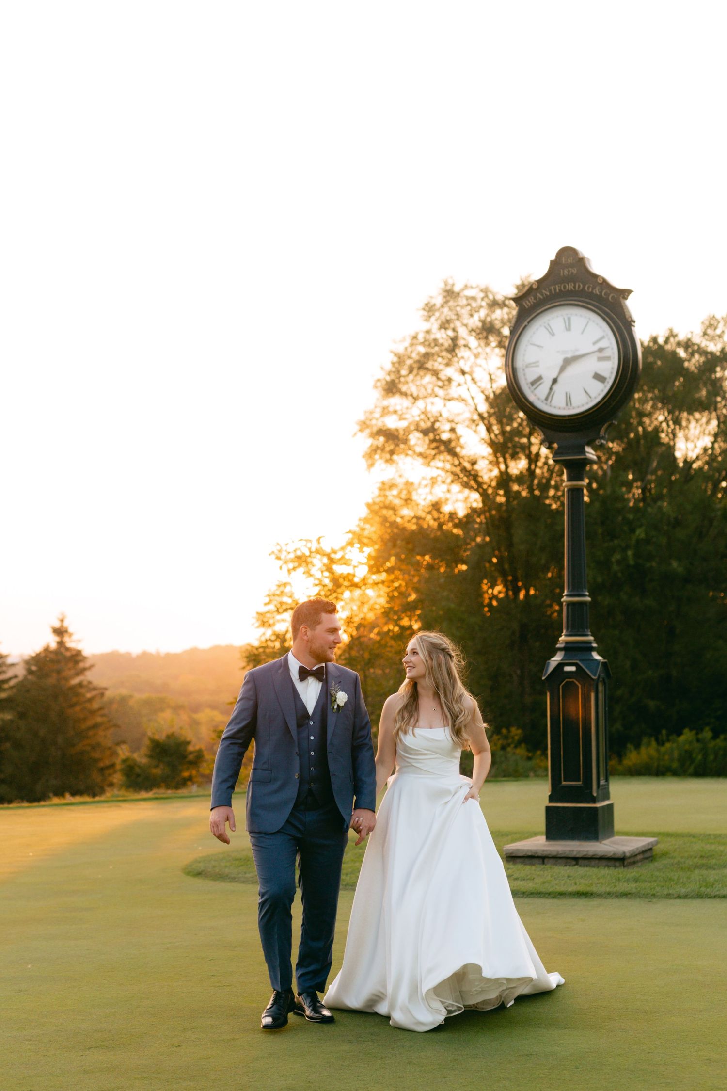 Wedding couple strolls together on manicured golf course greens at dusk.