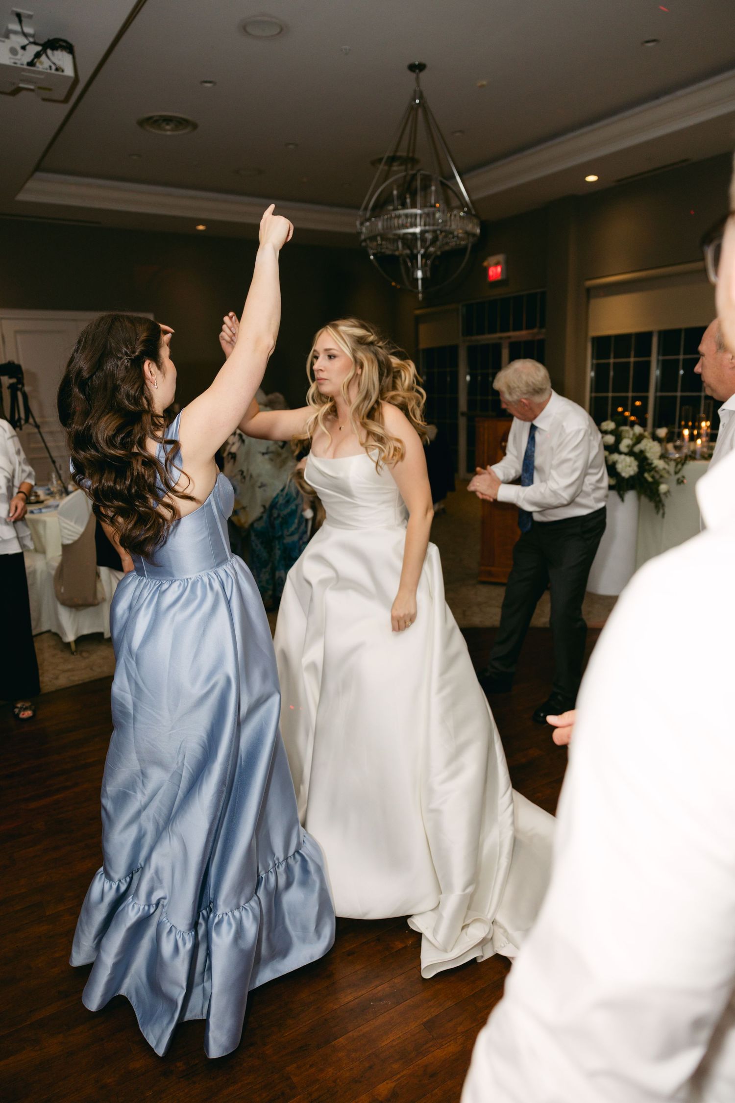 Wedding guests dancing and celebrating on wooden dance floor at reception.