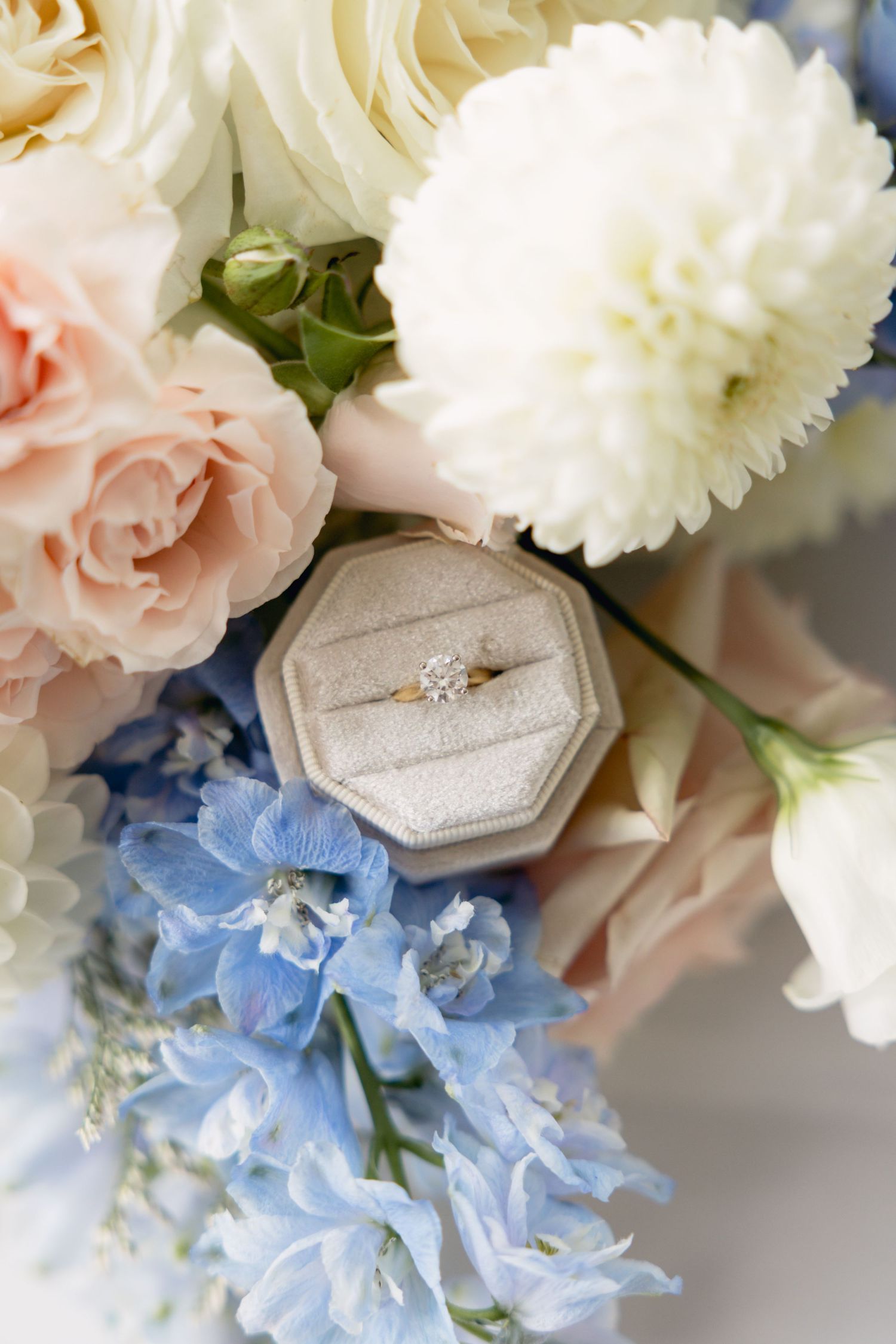 Wedding bouquet with blue hydrangeas, white carnations, and pink roses next to a hexagonal ring box.