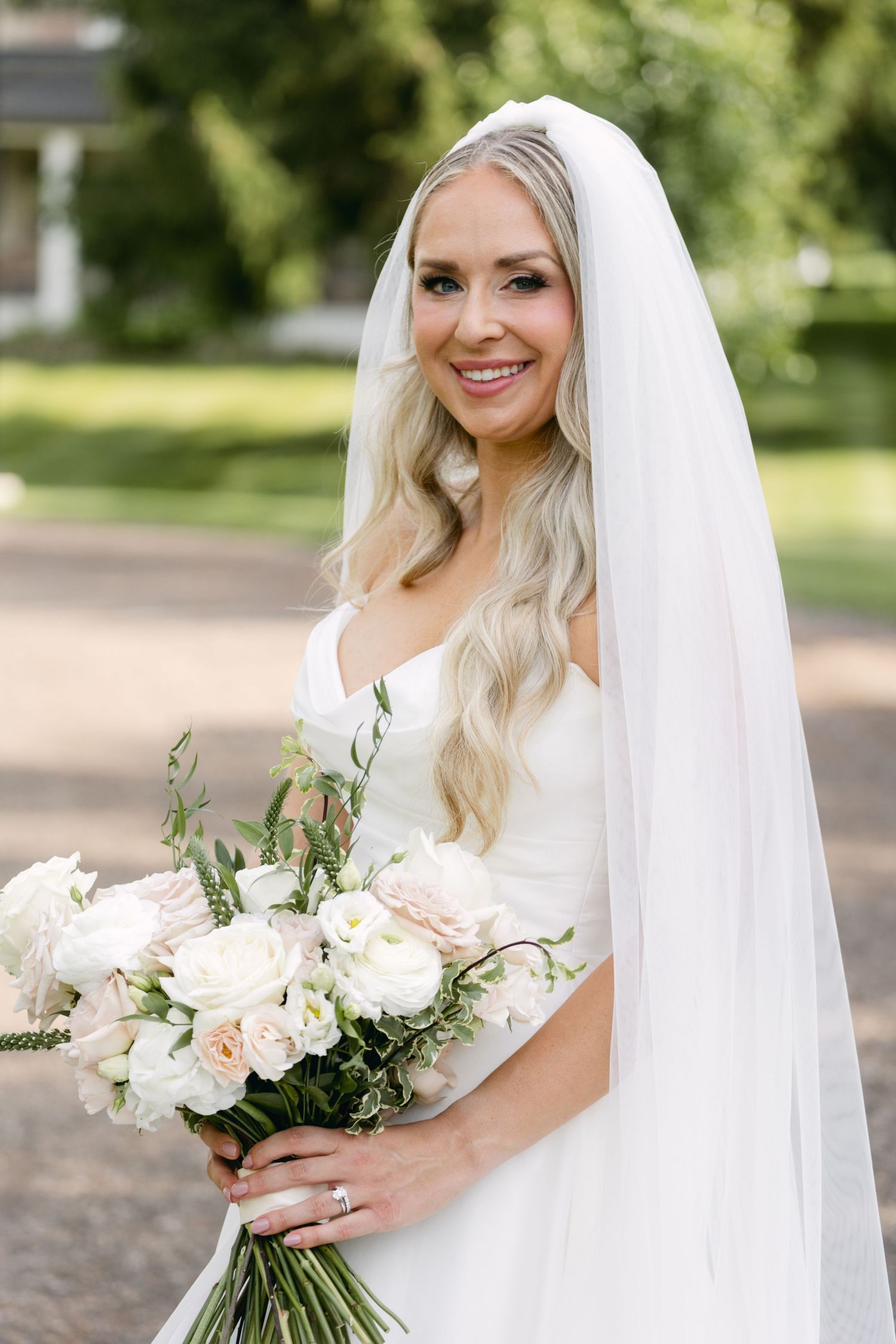 Bride holds elegant bouquet of white and blush roses with flowing veil.
