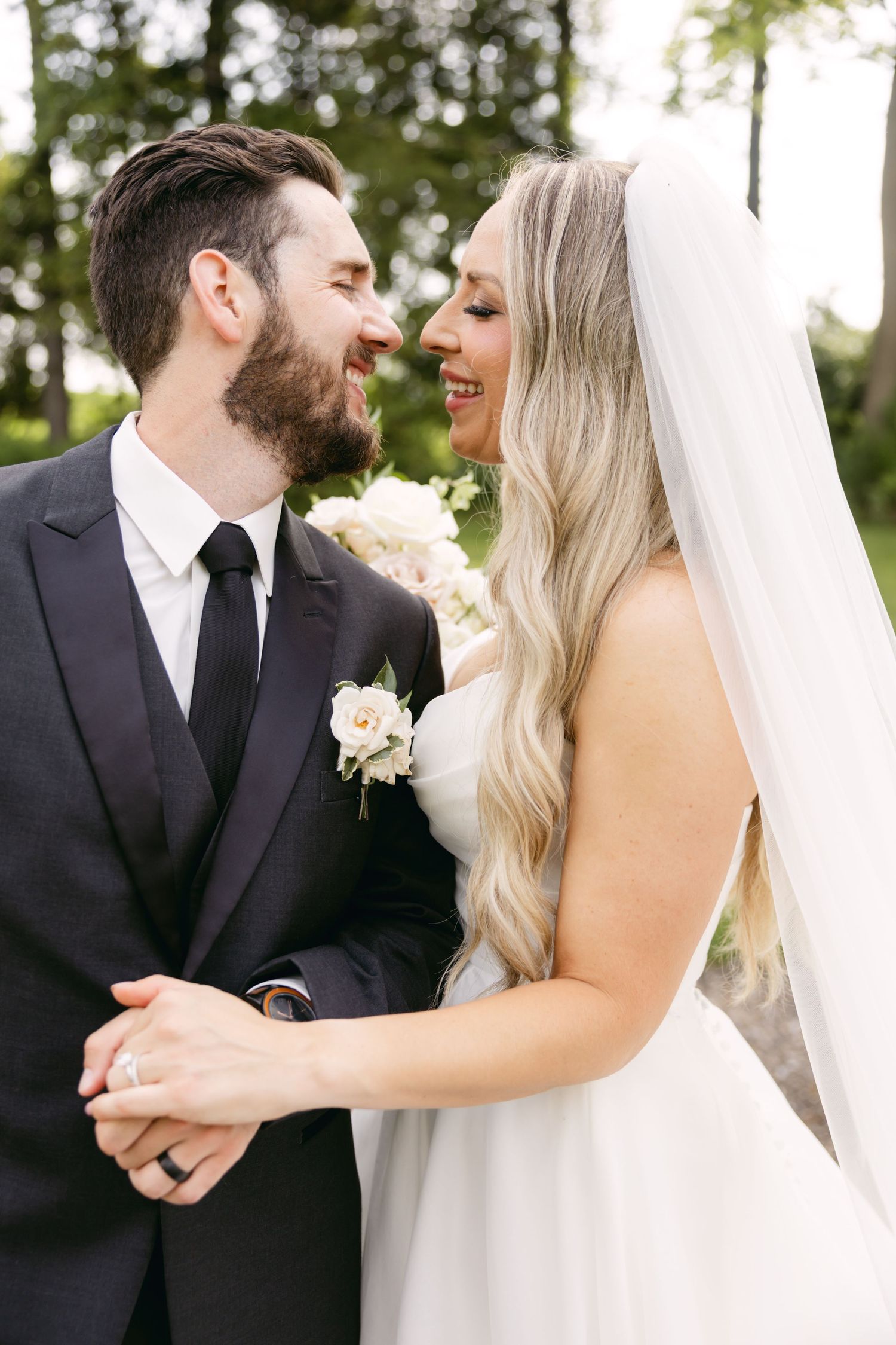 An intimate moment between newlyweds sharing laughter during their wedding portraits outdoors.