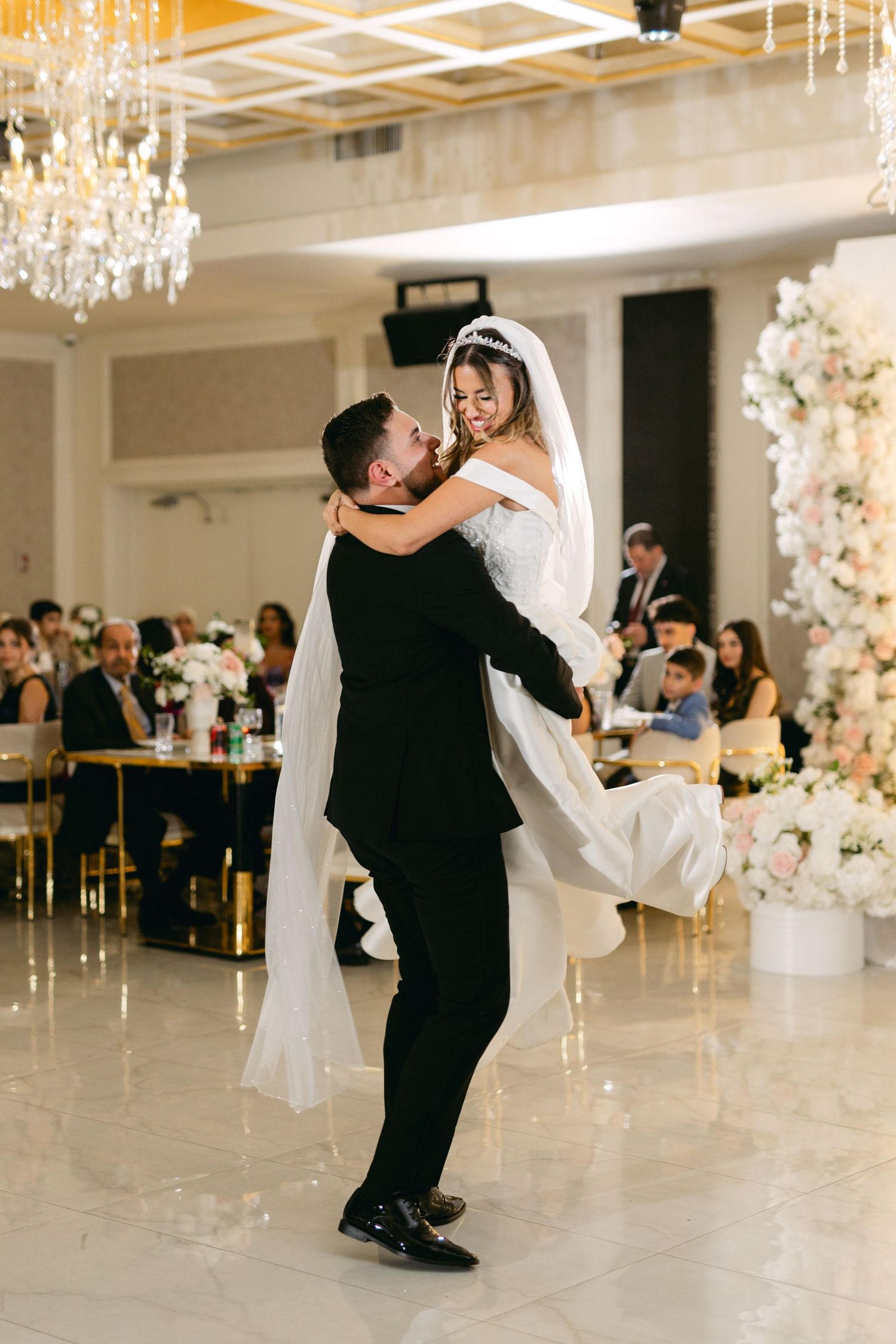 Wedding guests watch as the couple performs their first dance in an elegant white ballroom.