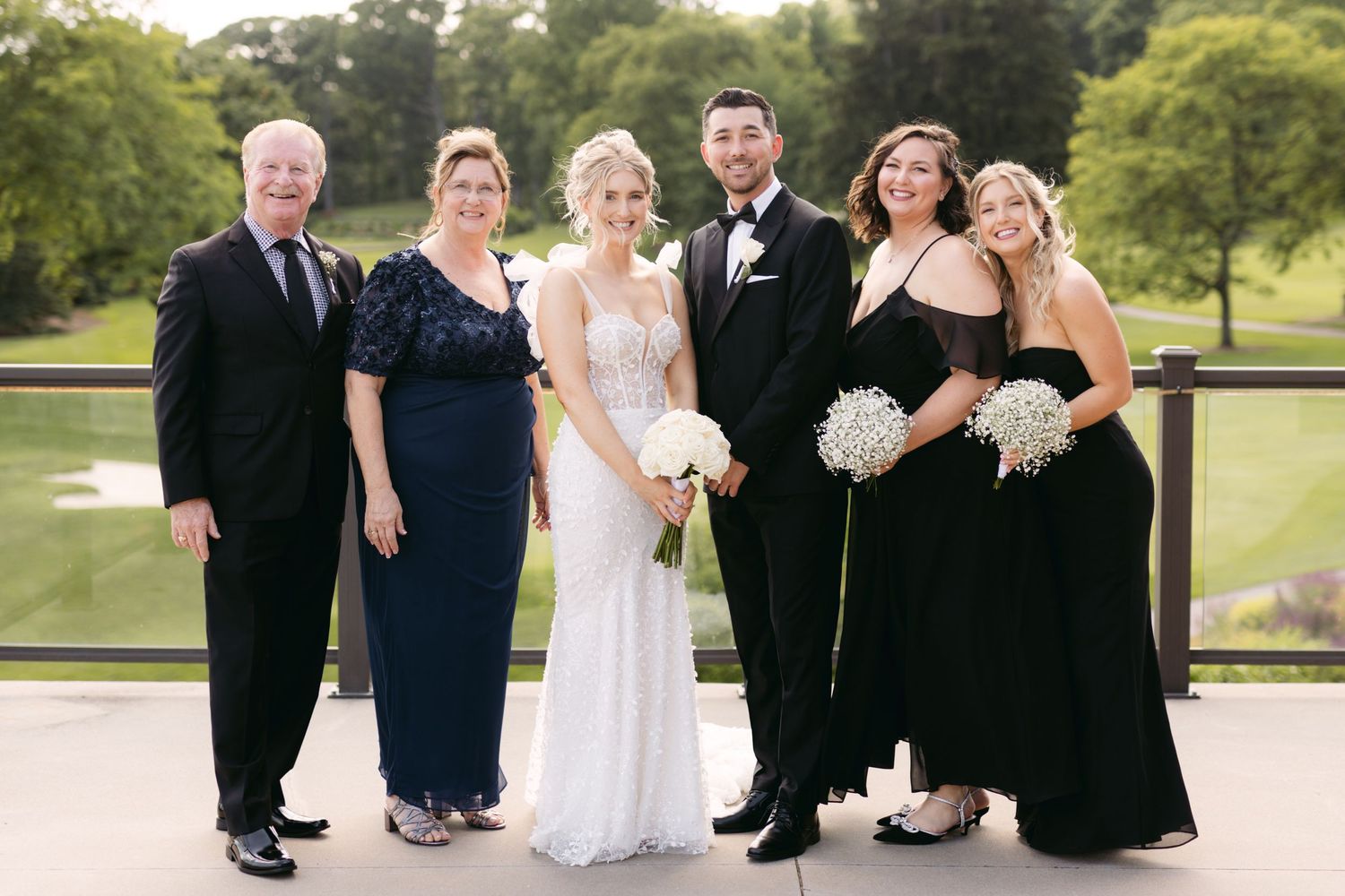 Formal wedding party group shot outdoors with scenic golf course view in background.