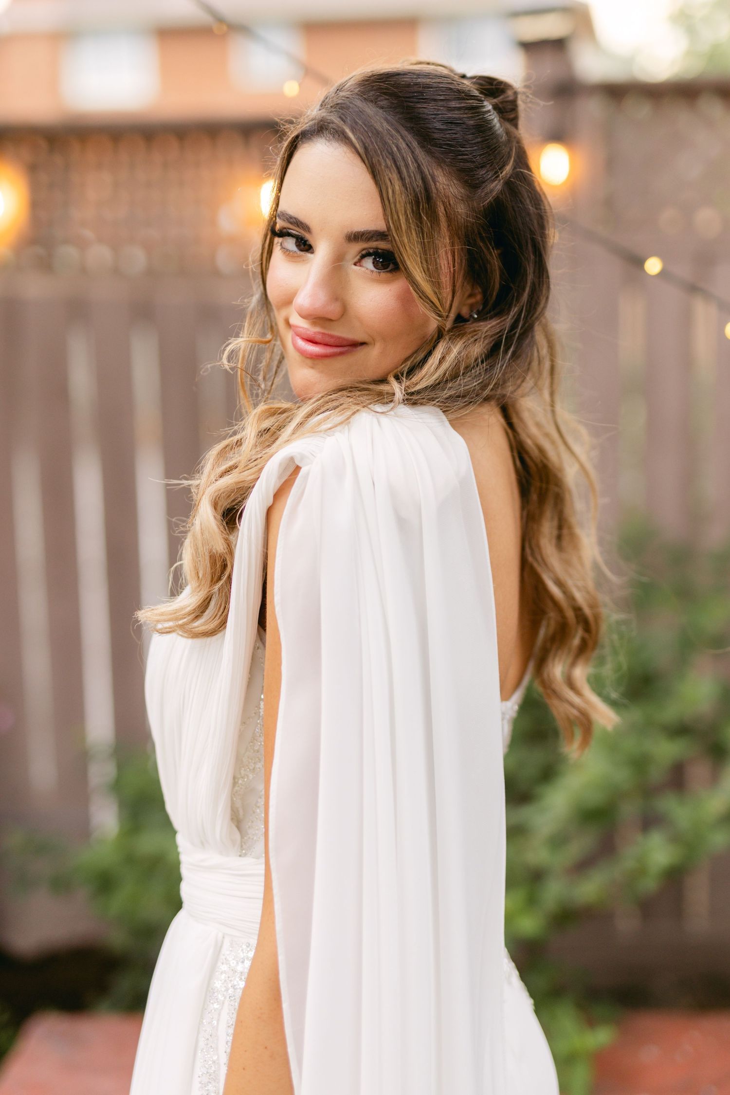 Close-up portrait of bride wearing white dress and red lipstick in outdoor setting.