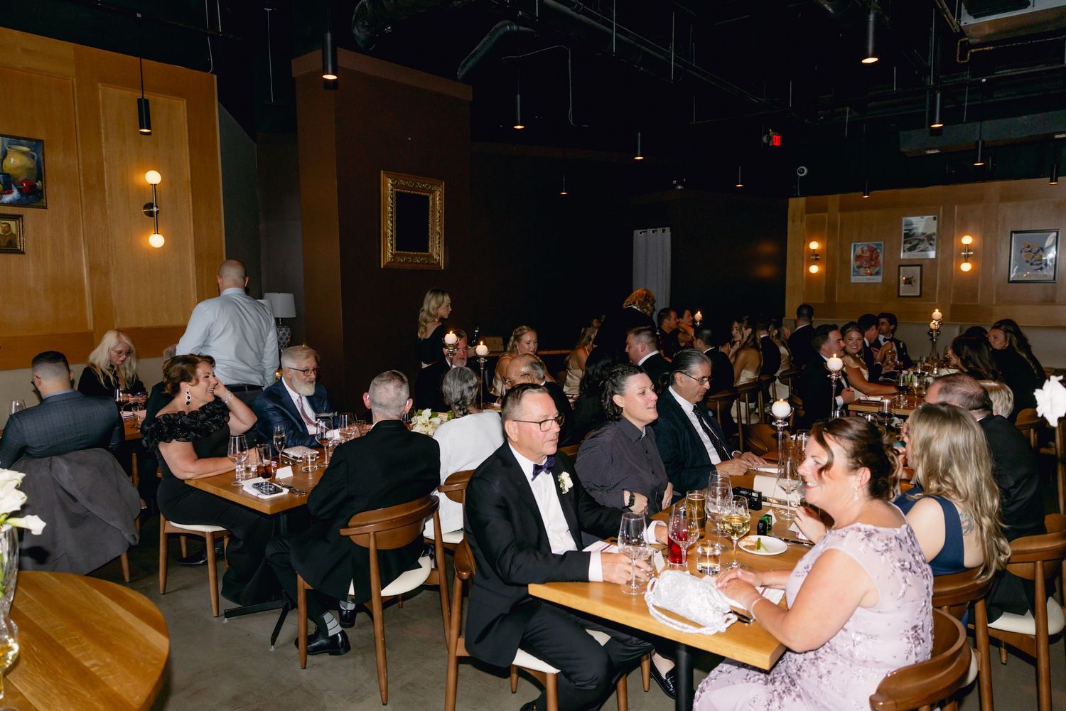 Wedding reception guests seated at candlelit tables in warmly lit restaurant dining room.