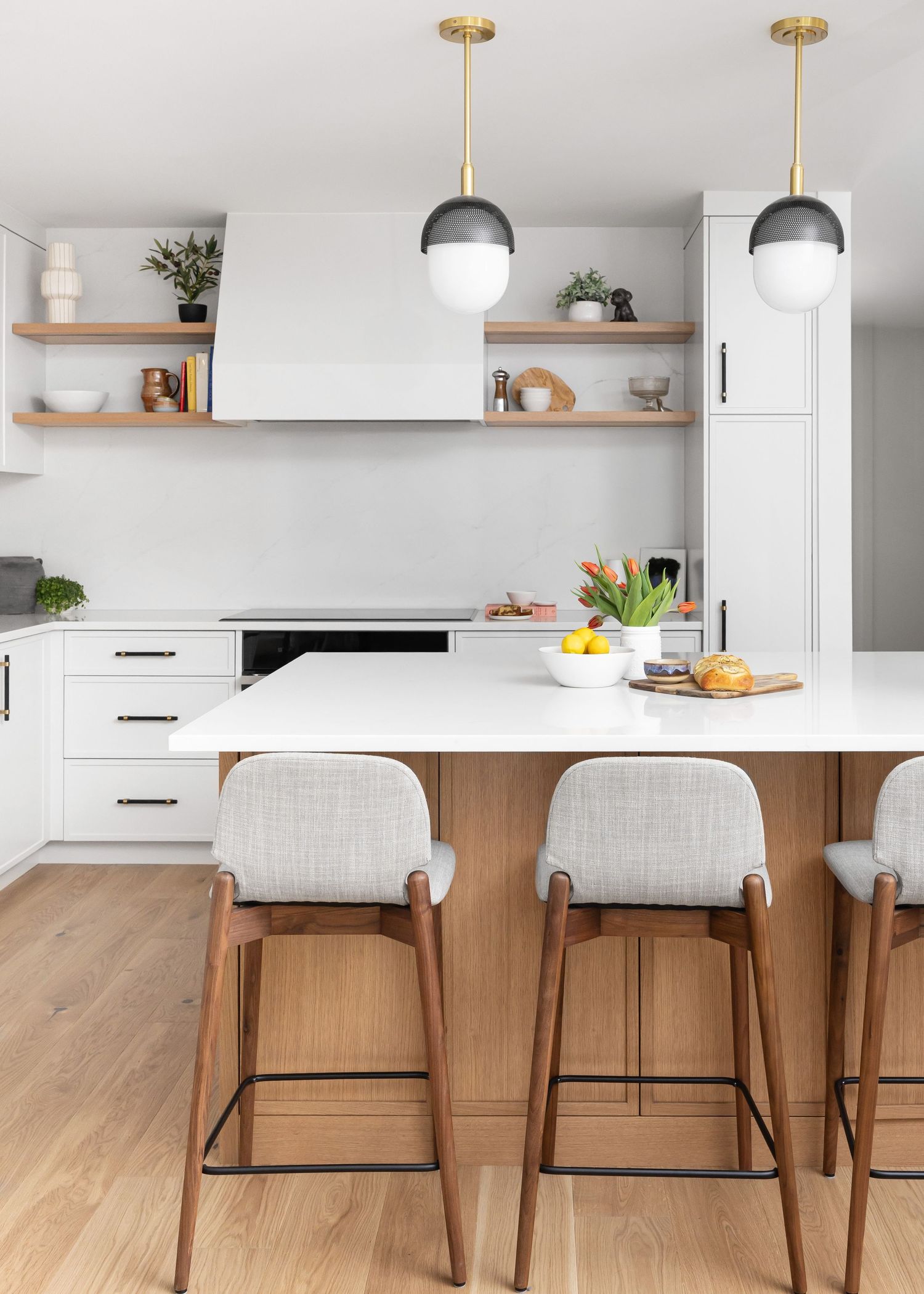 Minimalist kitchen featuring white cabinets, globe pendant lights, and upholstered bar stools.