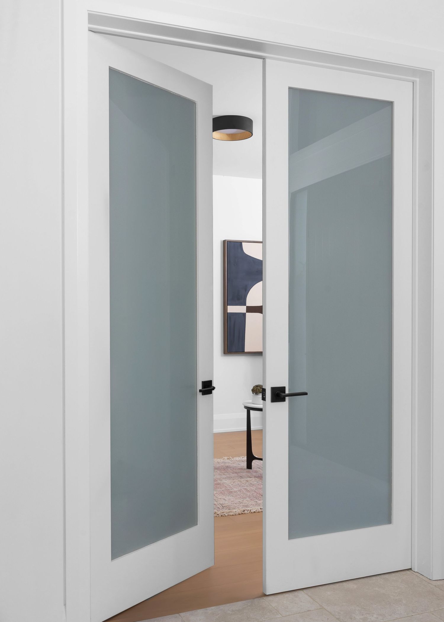 Sleek white hallway with frosted glass panel doors and modern black hardware.