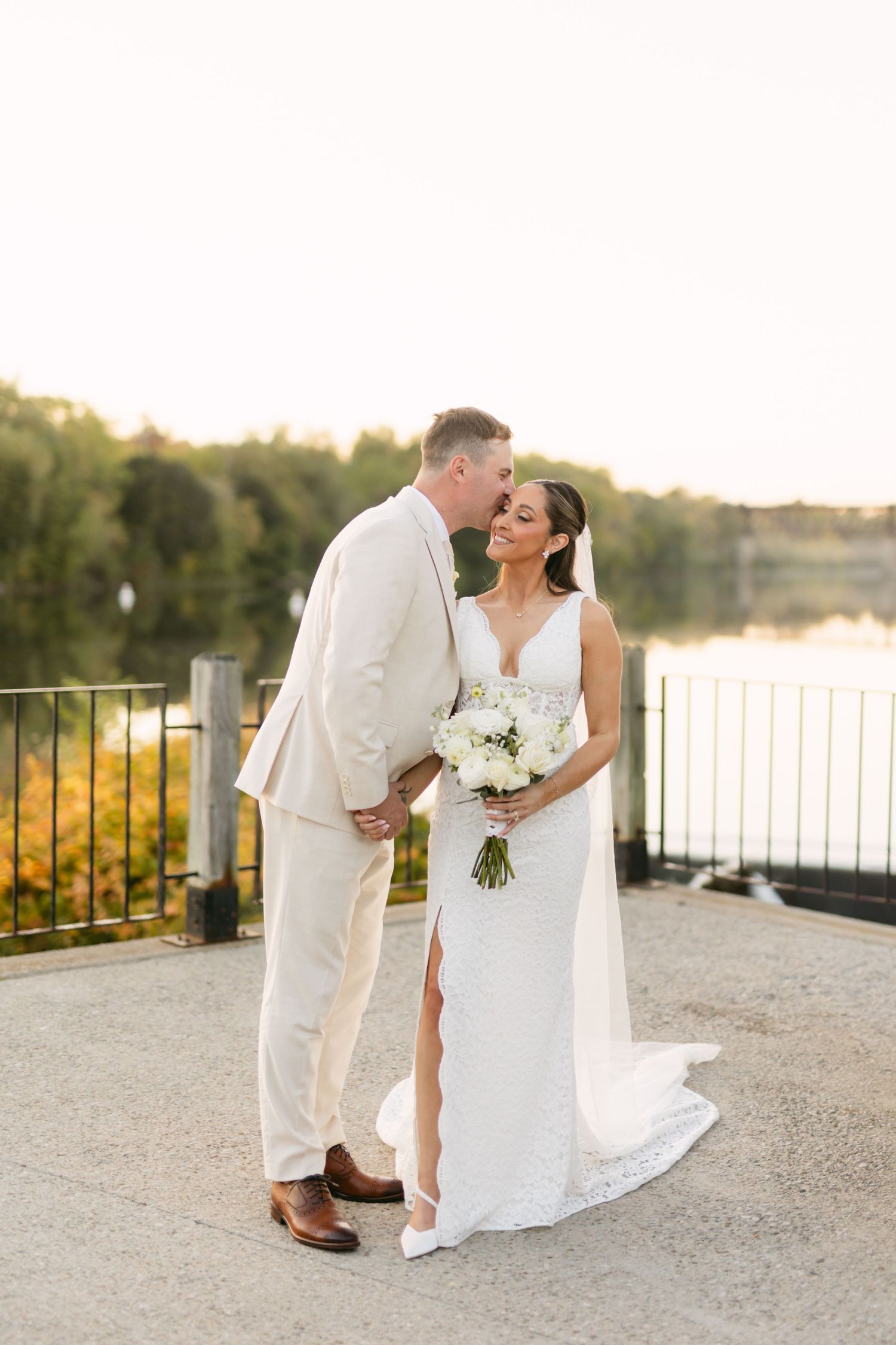 Elegant wedding couple poses against lakeside backdrop at sunset.