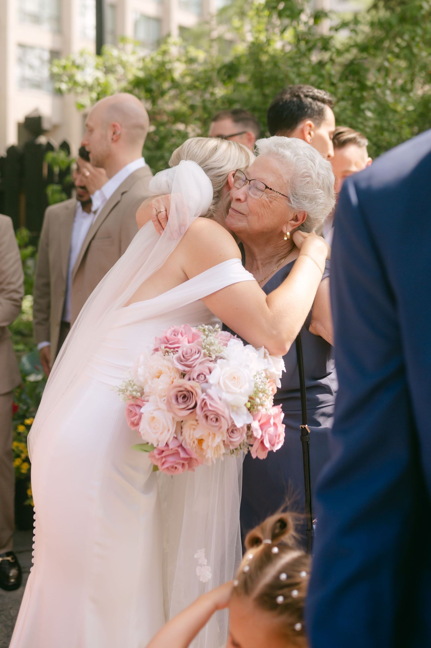 Emotional embrace during outdoor wedding ceremony with pink rose bouquet.