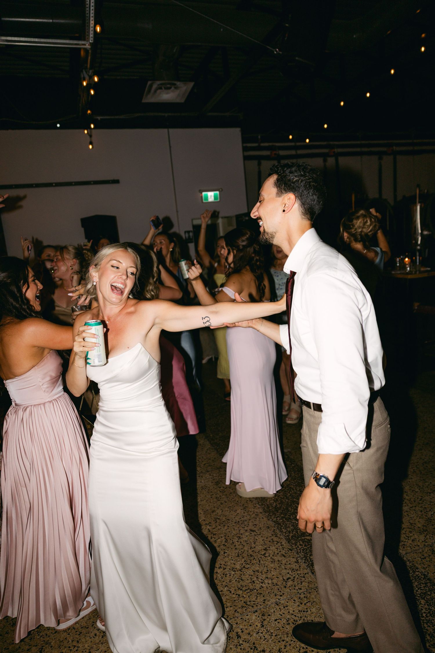 Wedding party dancing and celebrating on a dark dance floor with ambient lighting.