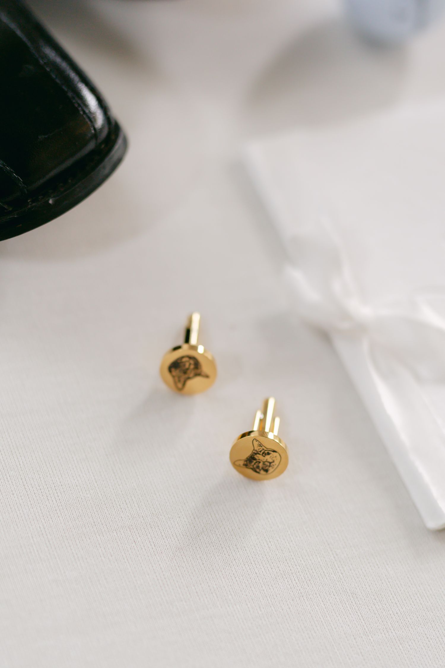 Close-up detail shot of gold cufflinks on white linen tablecloth.