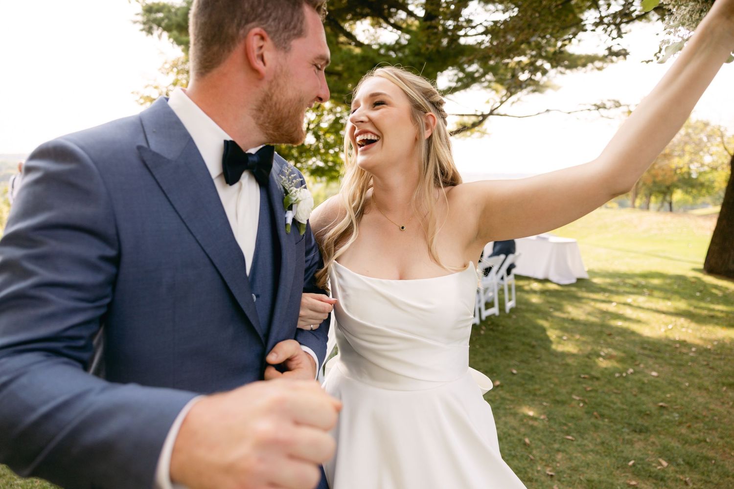 Joyful wedding couple celebrating outdoors with natural lighting and greenery in the background.