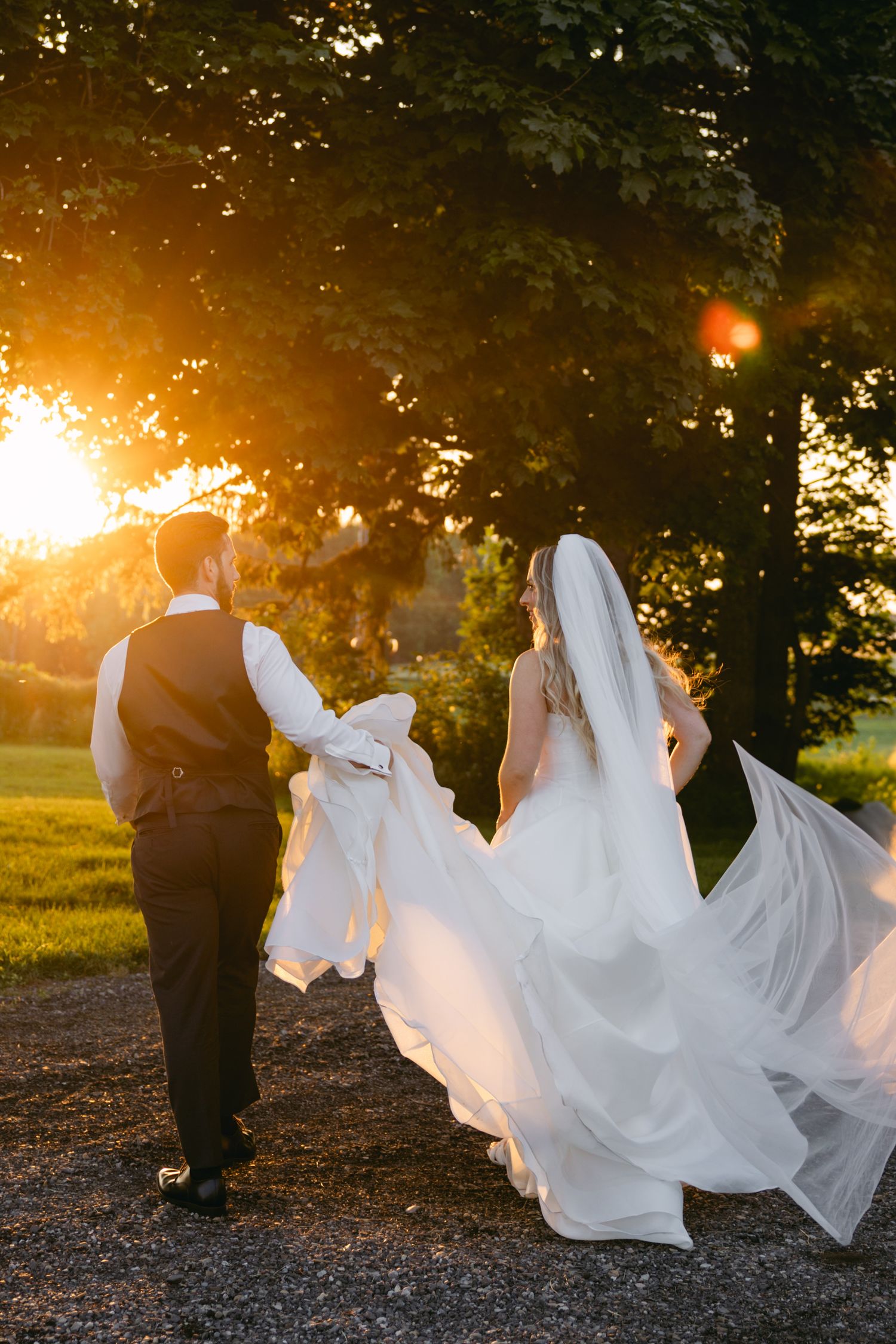Wedding couple poses at sunset with flowing white dress creating dramatic silhouettes against golden light.