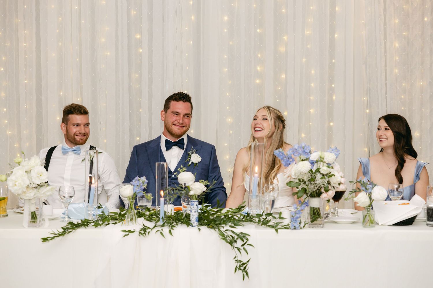 Wedding reception head table decorated with white flowers and blue accents.