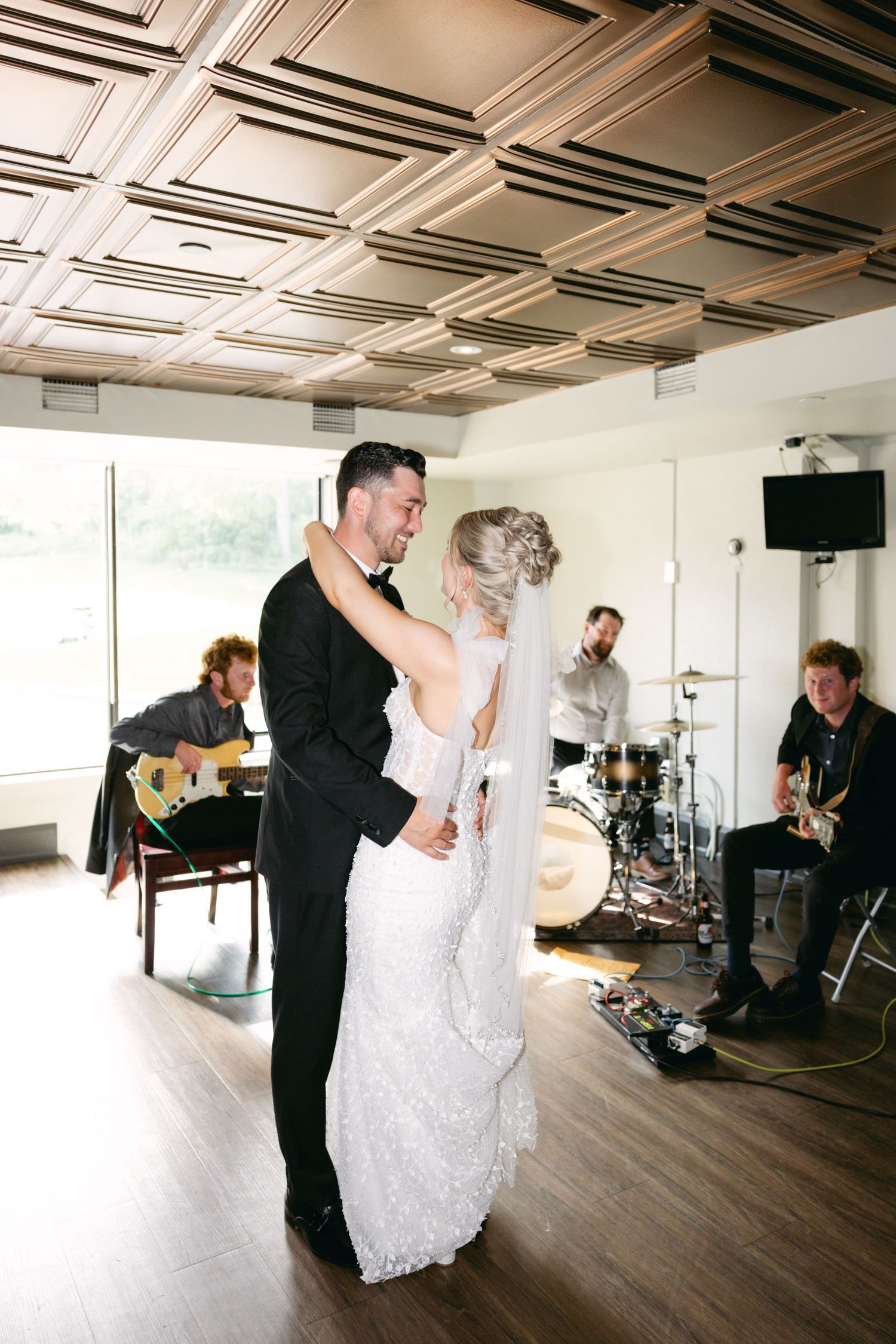 Couple shares first dance while band performs in modern indoor venue.