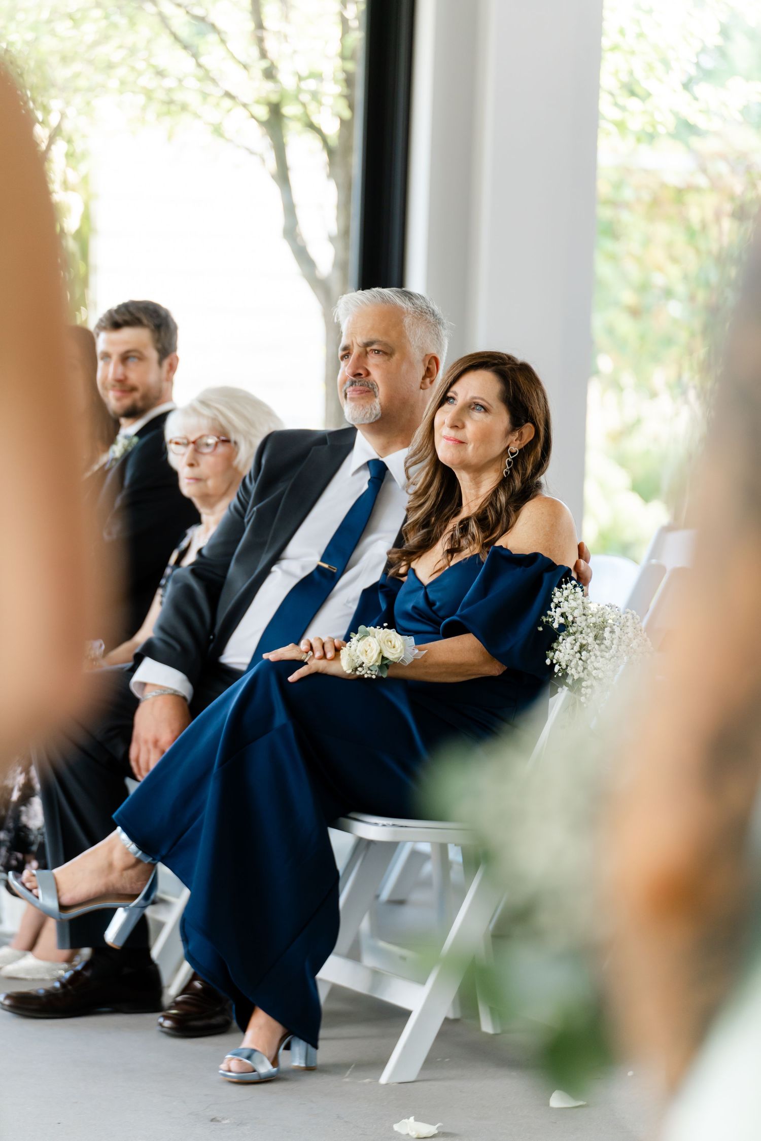 Wedding guests seated in formal attire at outdoor covered venue.