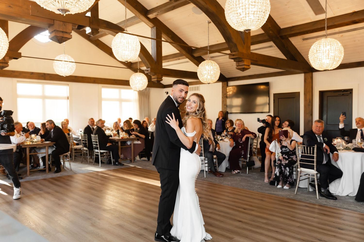 Wedding couple shares first dance in rustic venue with crystal chandeliers.