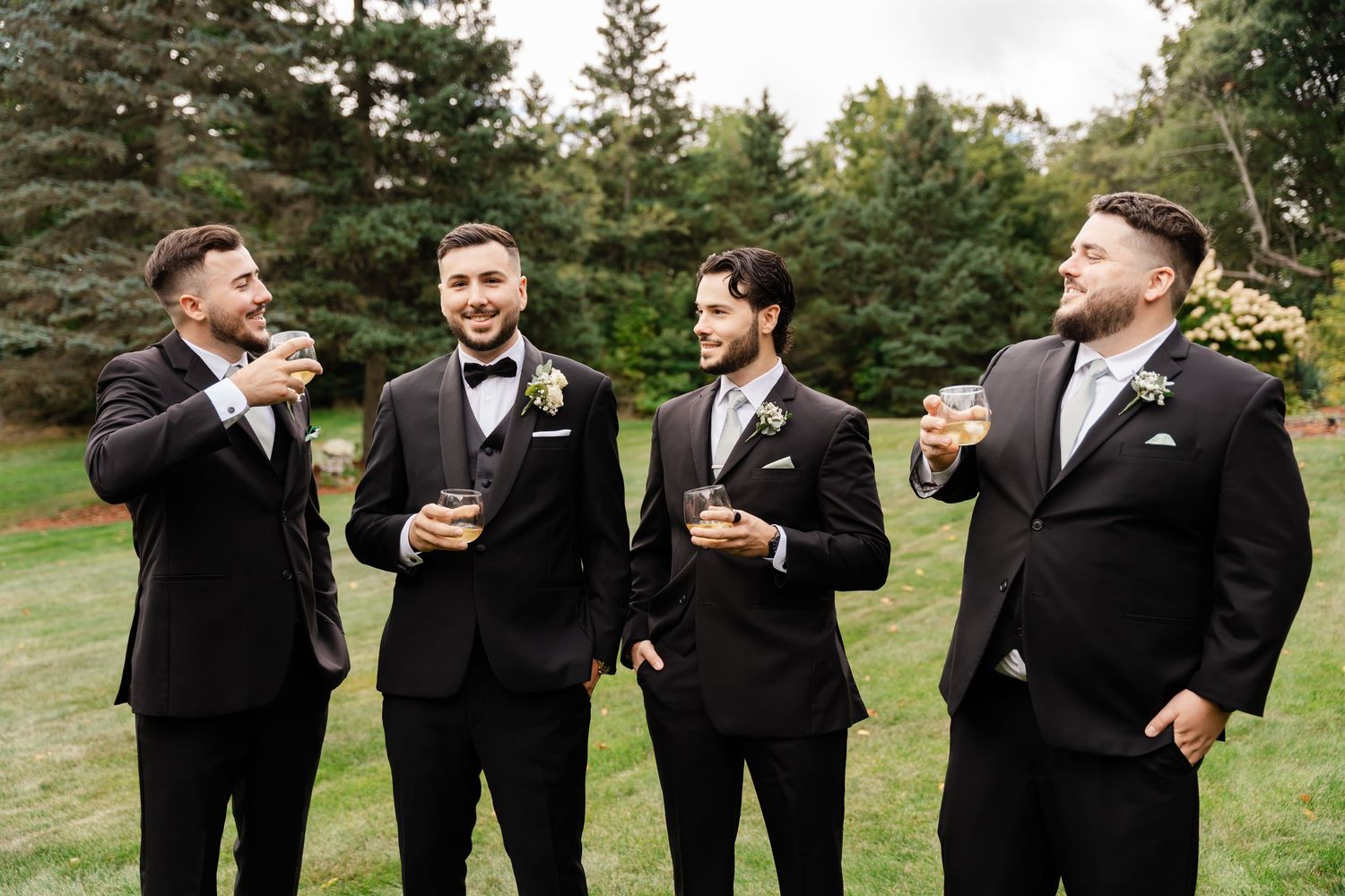 Wedding party in black tuxedos laughing and enjoying candid moments outdoors.
