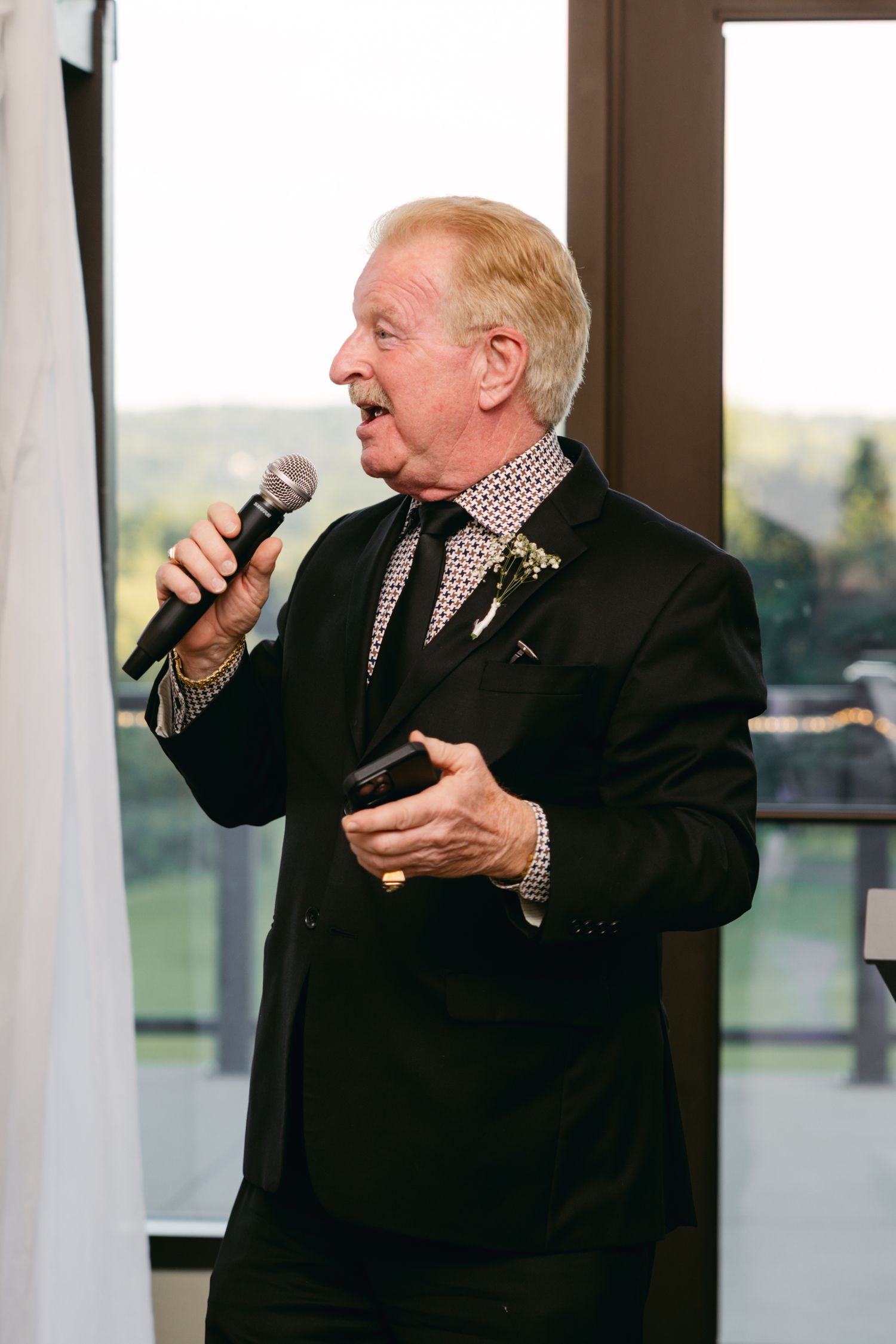 Wedding guest in formal attire passionately singing or speaking into a microphone.