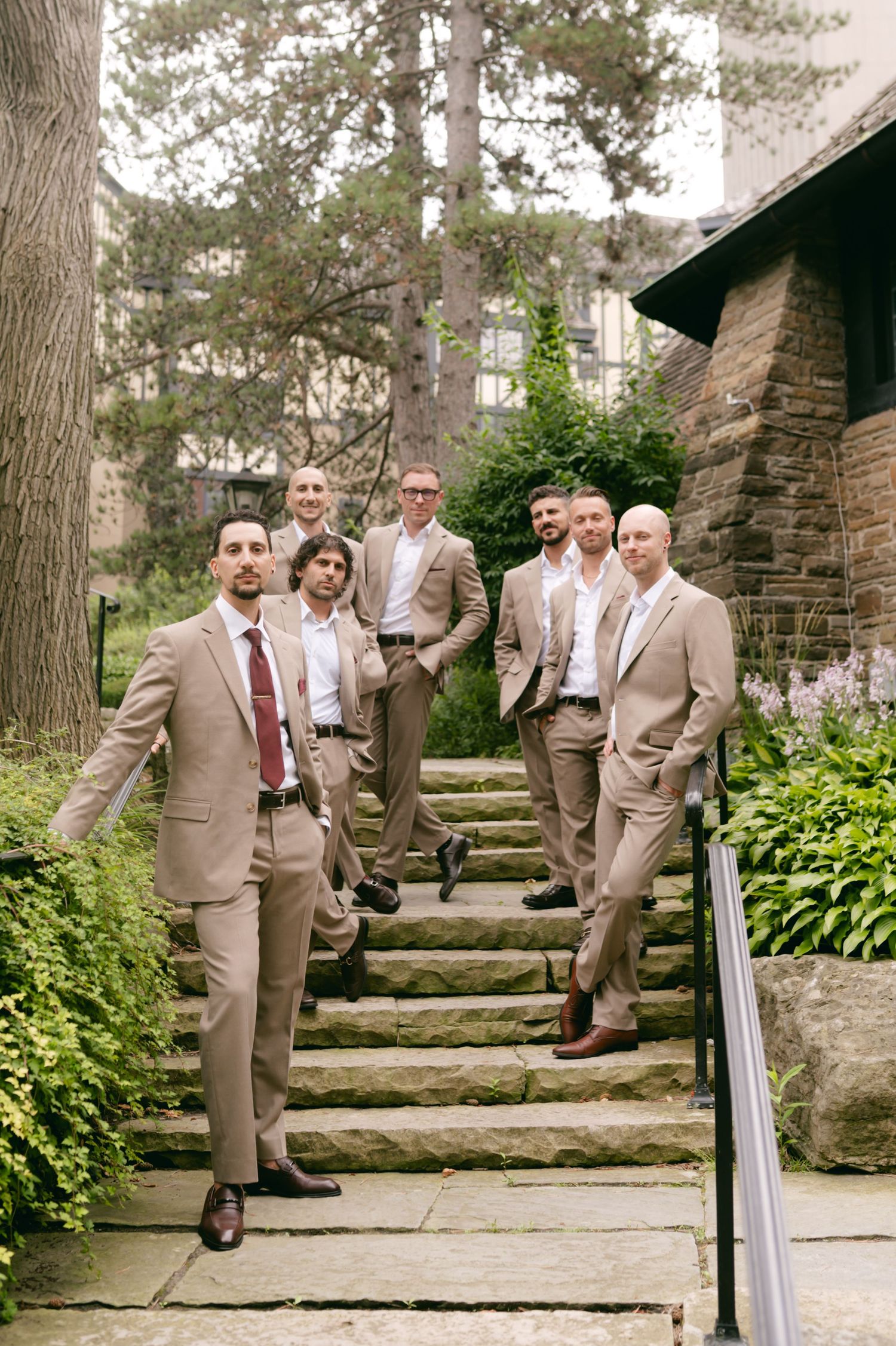 Wedding party members in tan suits descending stone garden steps.