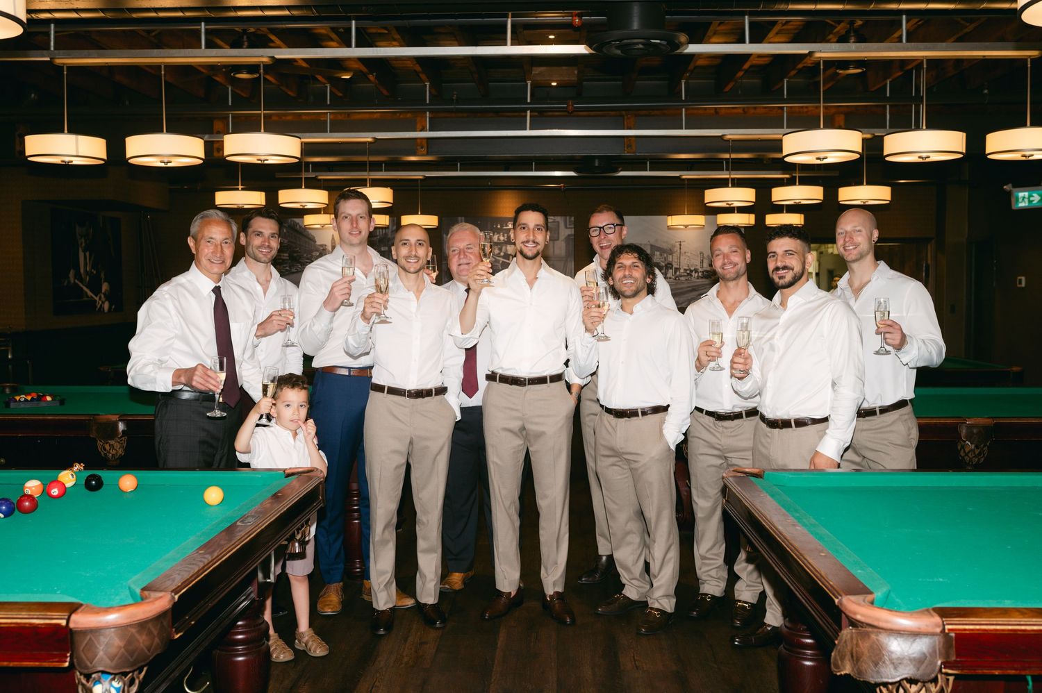 Groomsmen in light colored suits posing together at a pool table.