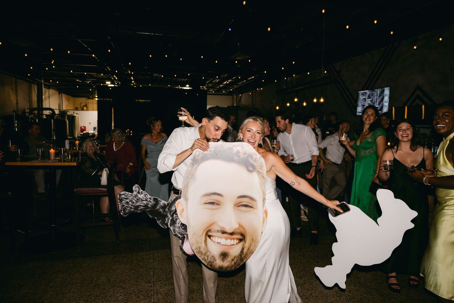 Dark reception venue with guests dancing and celebrating under dim lighting.