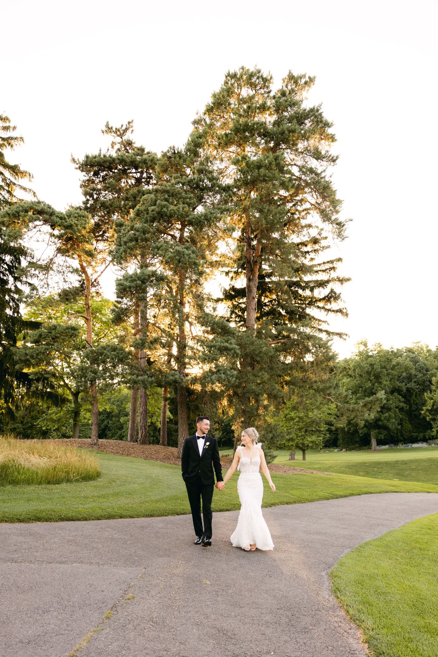 A couple strolls together on a winding path through a scenic golf course at sunset.
