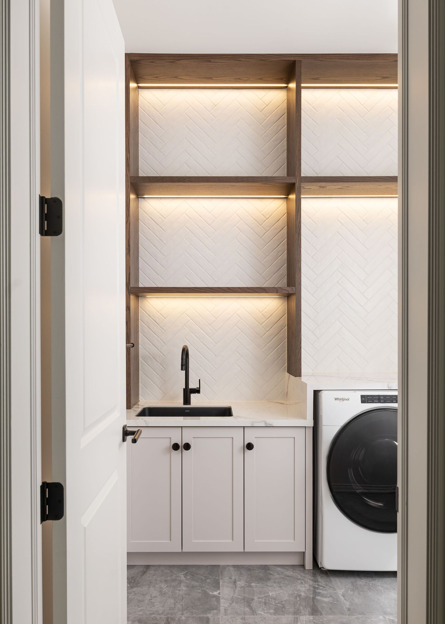 Modern white kitchen with backlit shelving, marble backsplash, and sleek appliances.