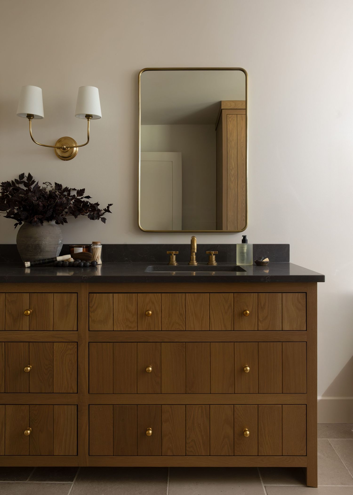 Custom wood vanity with black countertop and brass hardware in bathroom.
