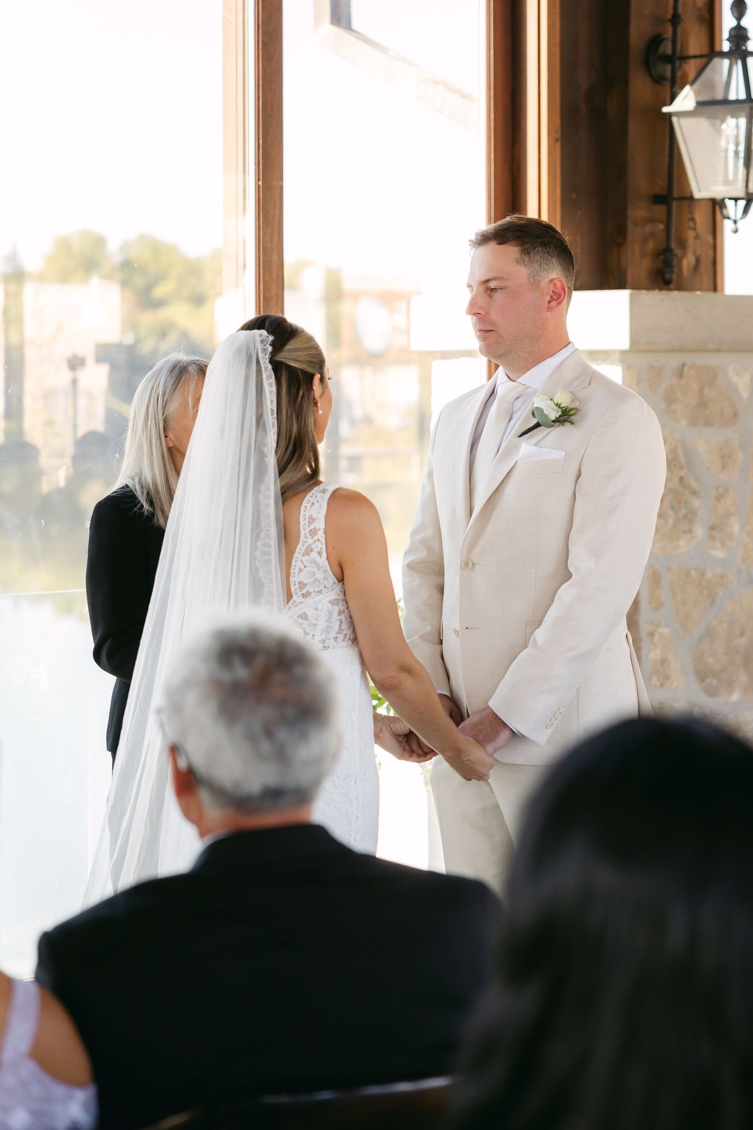 A wedding ceremony takes place in a sunlit venue with rustic wooden beams and stone walls.