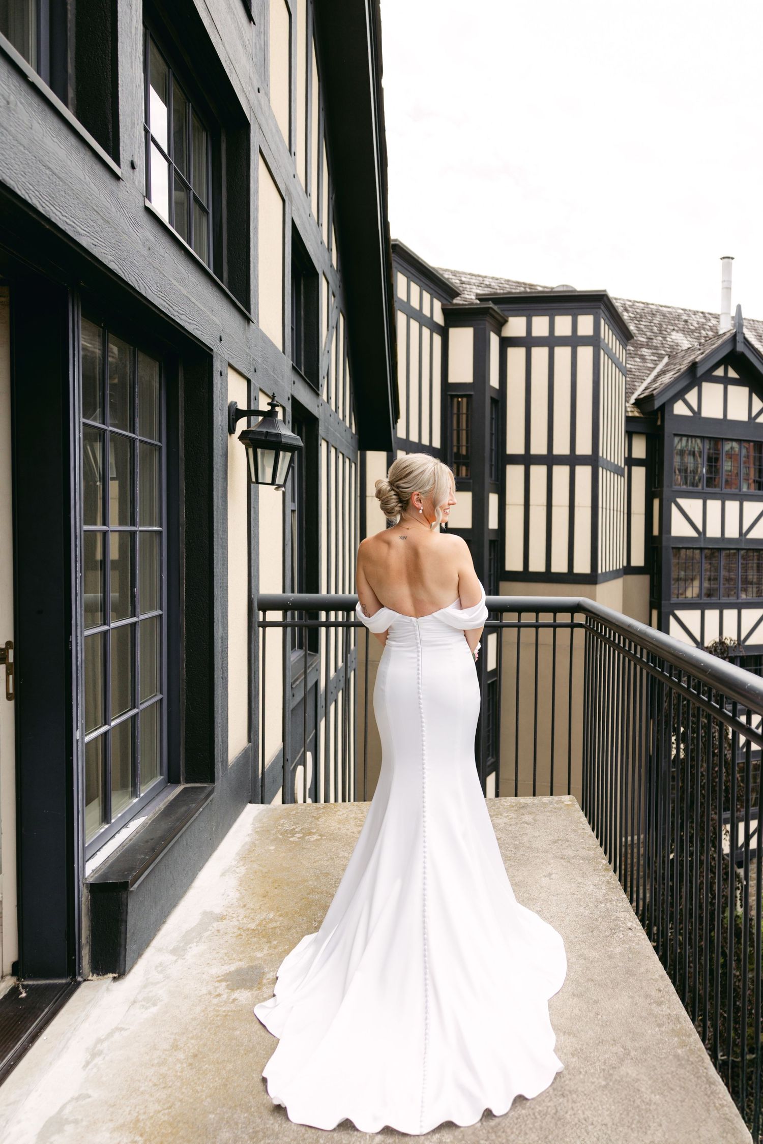 Back view of bride in elegant white gown standing in Tudor-style building hallway.
