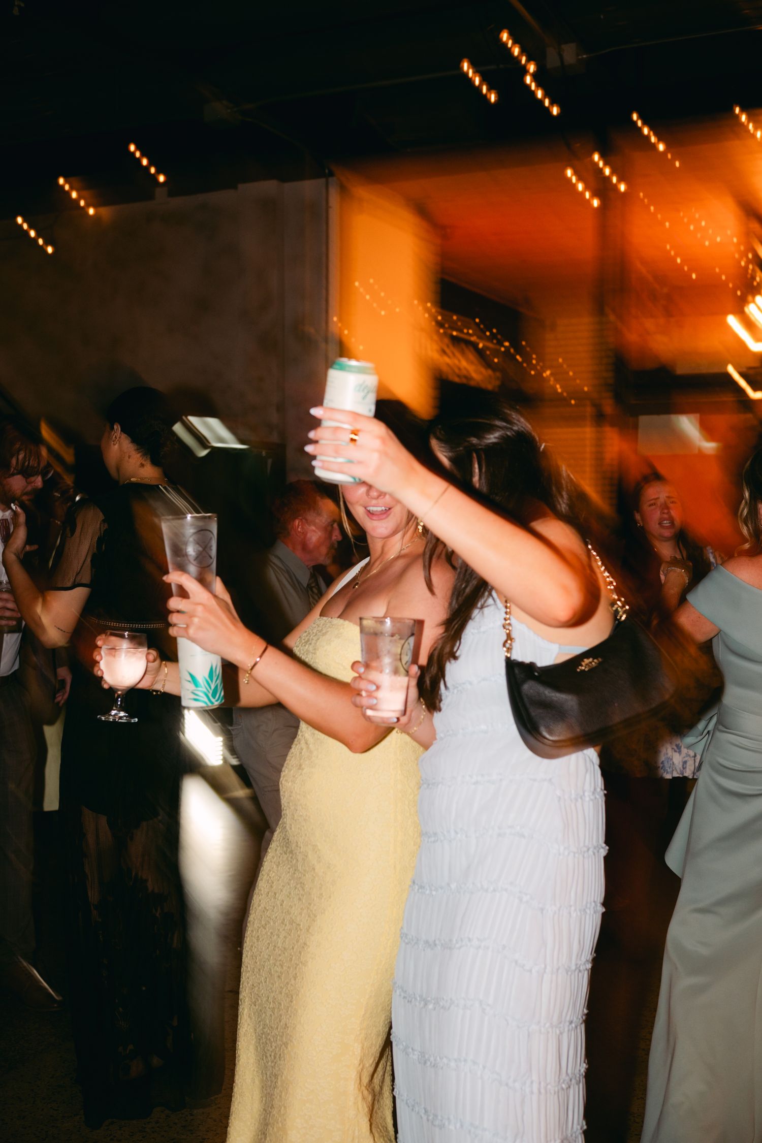 Wedding guests dancing with raised arms under warm ambient lighting.