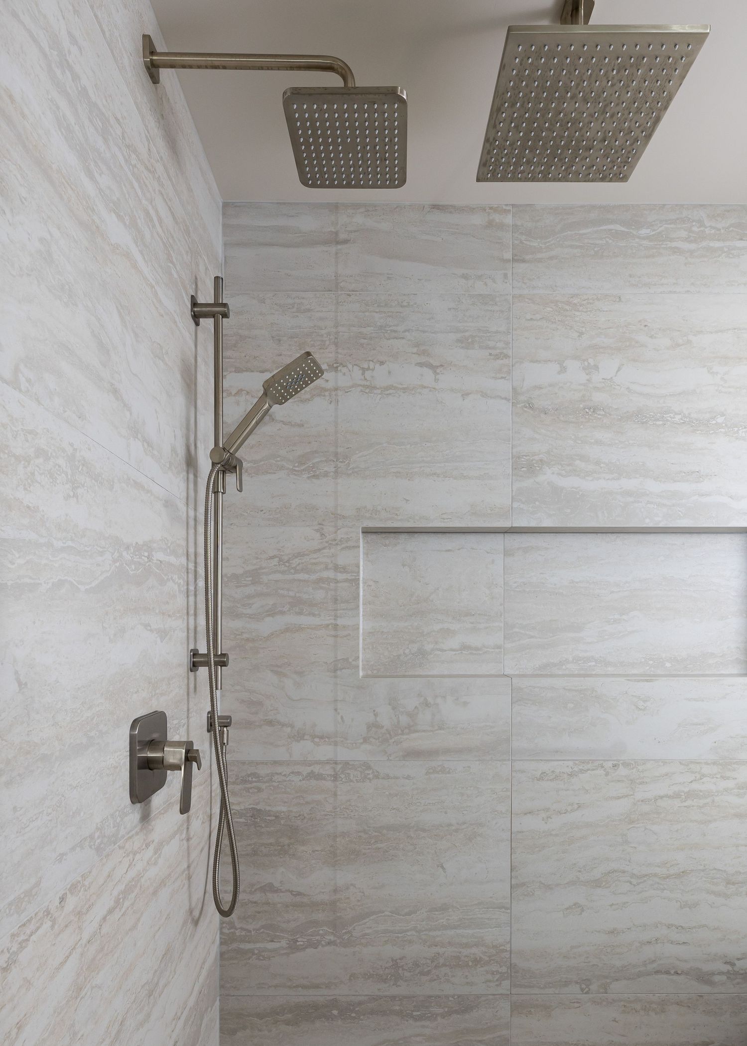 Luxury shower interior with multiple rainfall showerheads and light marble tile walls and floor.
