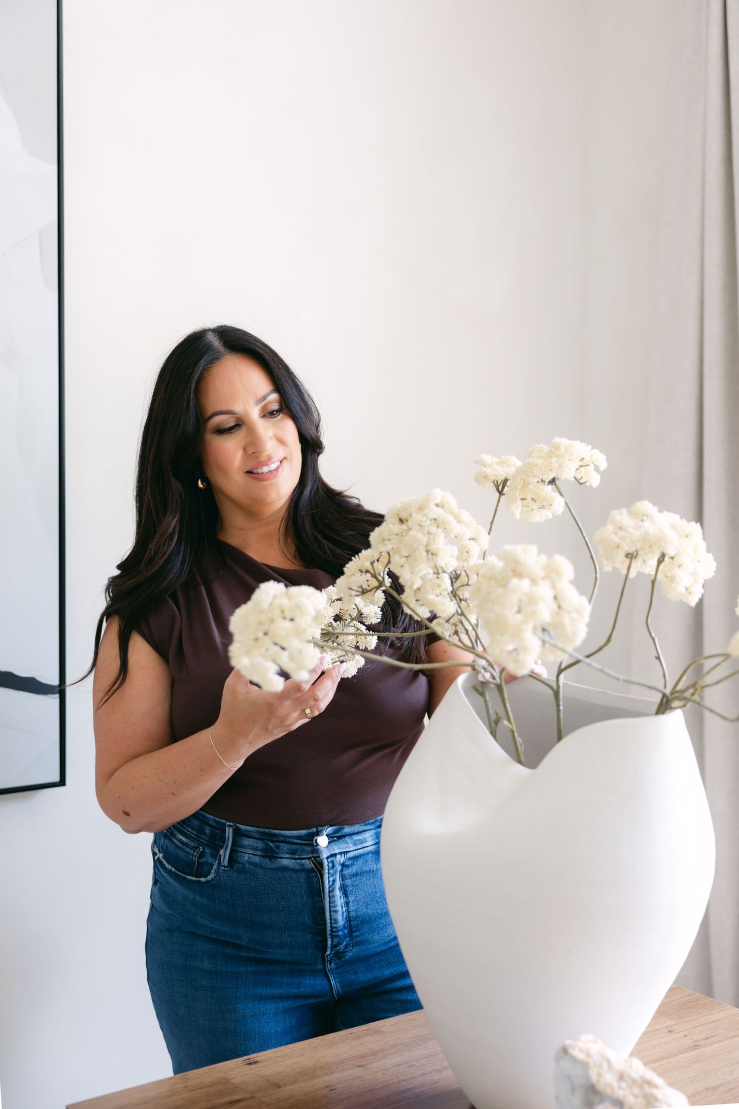 Woman in dark top styling white orchids in contemporary white vase.