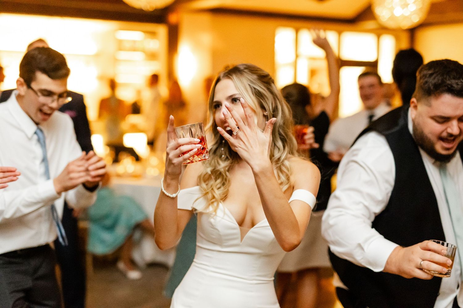 Wedding celebration with guests enjoying drinks and laughter at an indoor reception.