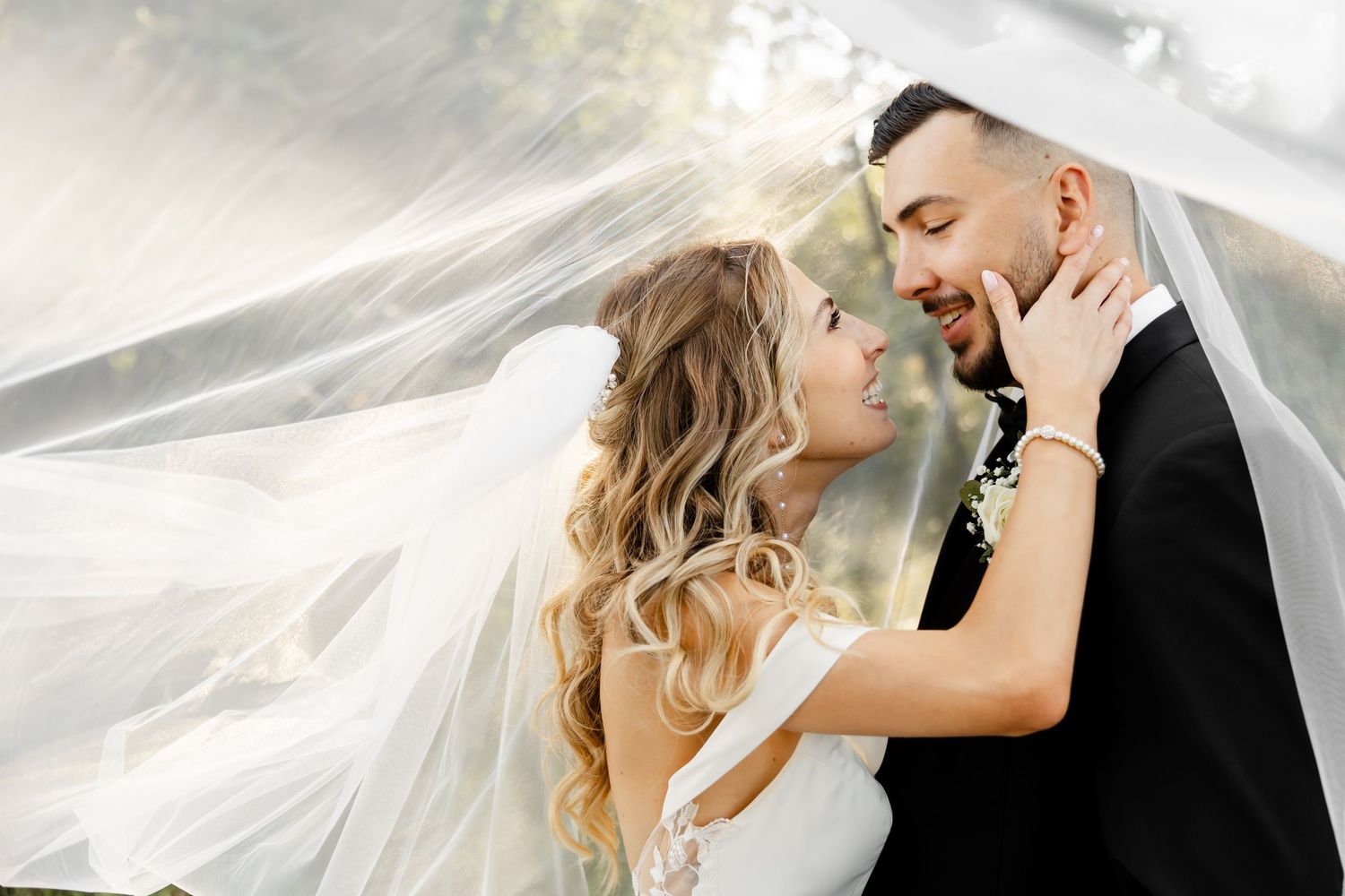A romantic wedding moment captured outdoors with a flowing veil and natural lighting.