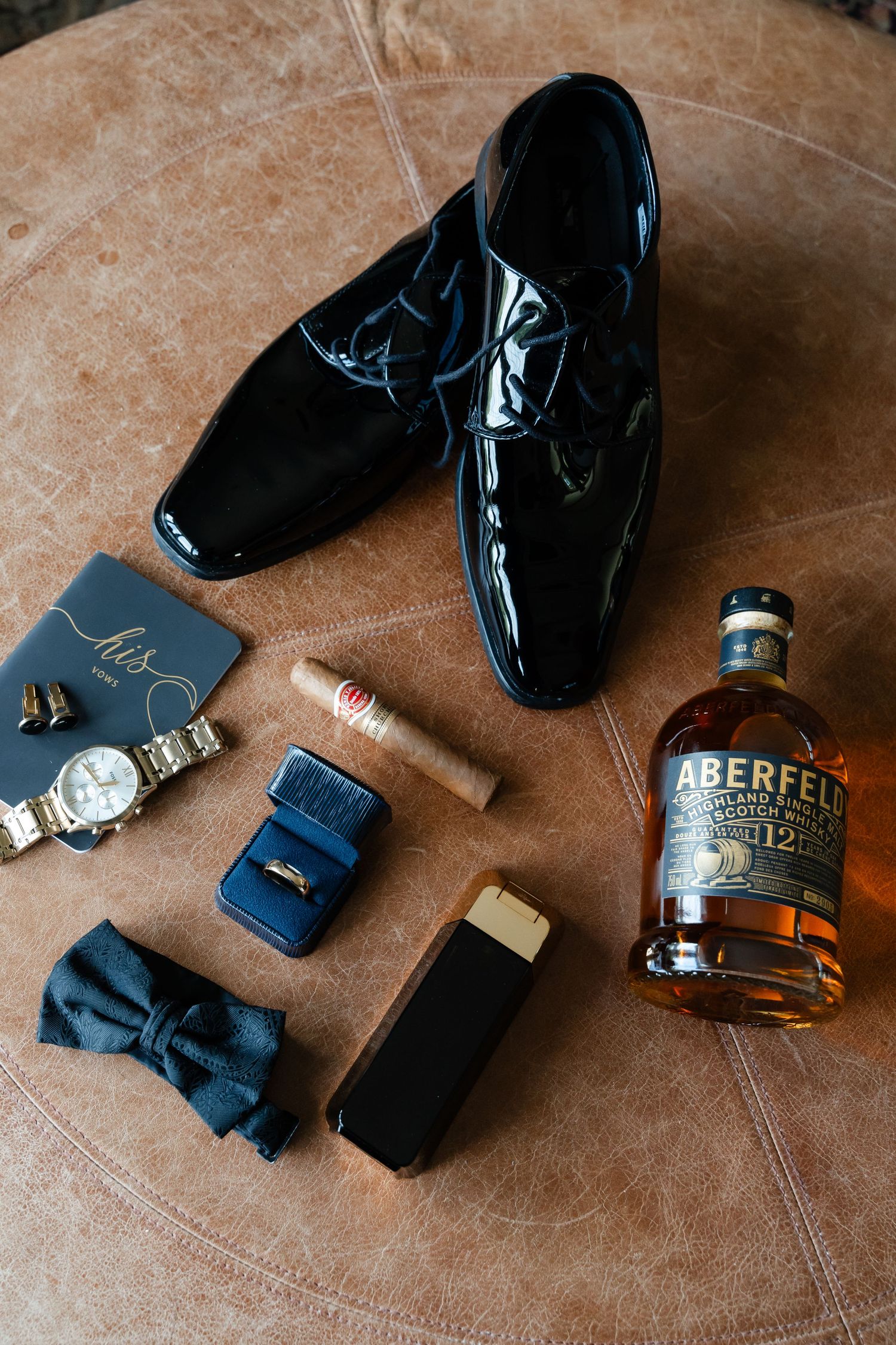 Wedding day accessories including dress shoes, watch, and a bottle of Aberfeldy whisky arranged on brown surface.