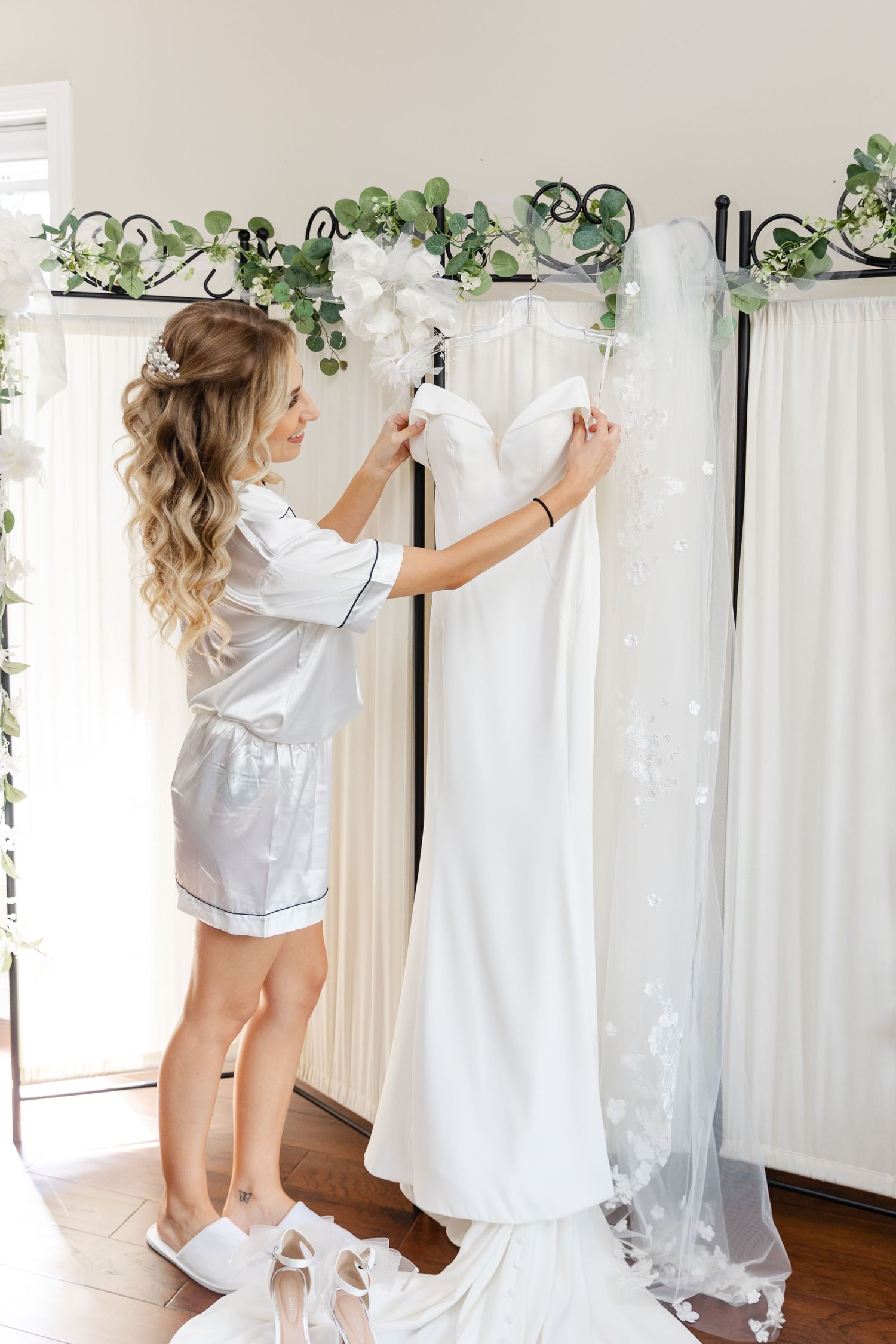 Getting ready for wedding day scene with white dress being steamed near decorative greenery.