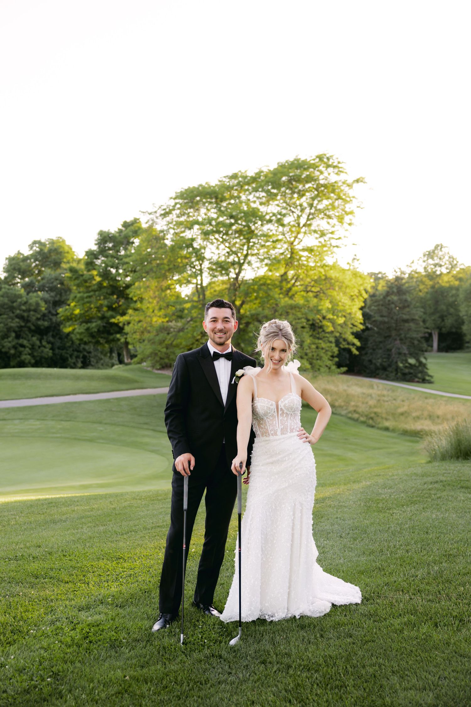 Wedding couple poses together on a beautiful golf course during golden hour.