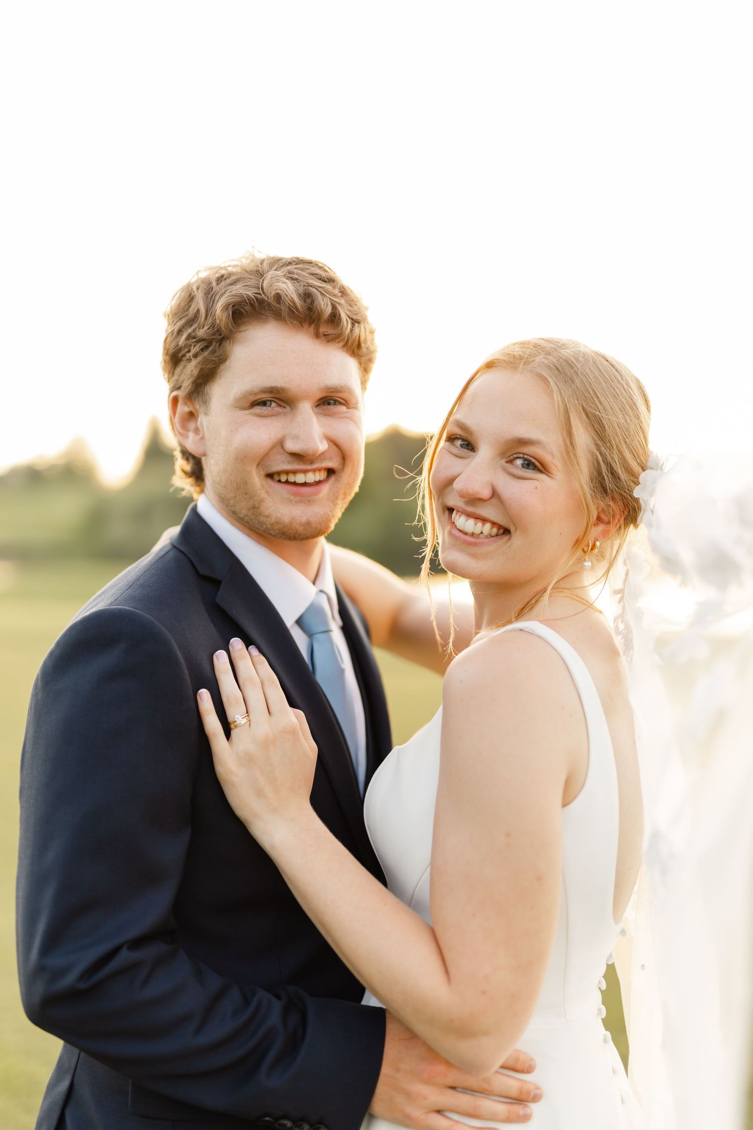A romantic wedding couple embraces in golden sunlight during their outdoor photo session.