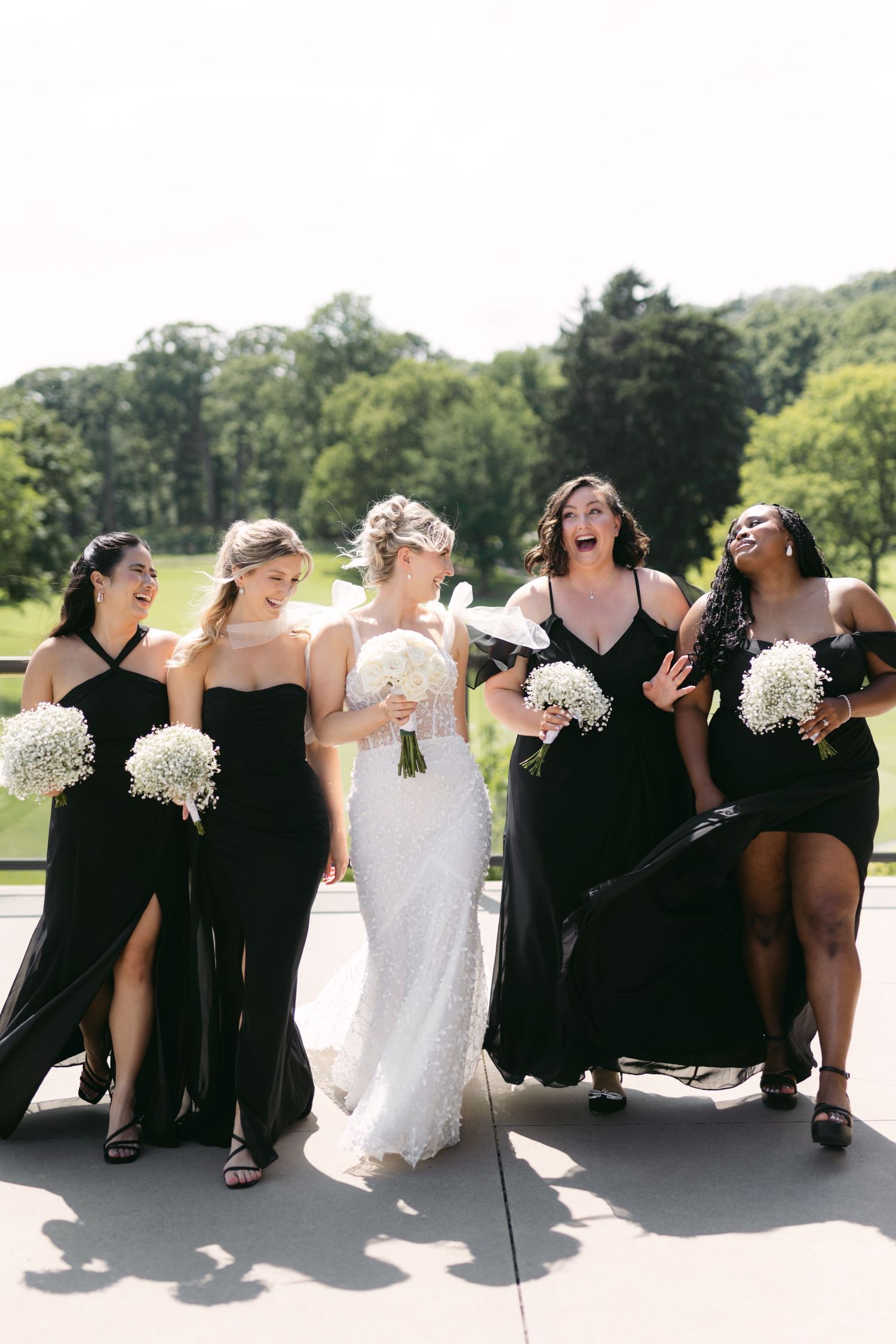 Wedding party in formal attire sits casually on outdoor patio with scenic golf course backdrop.