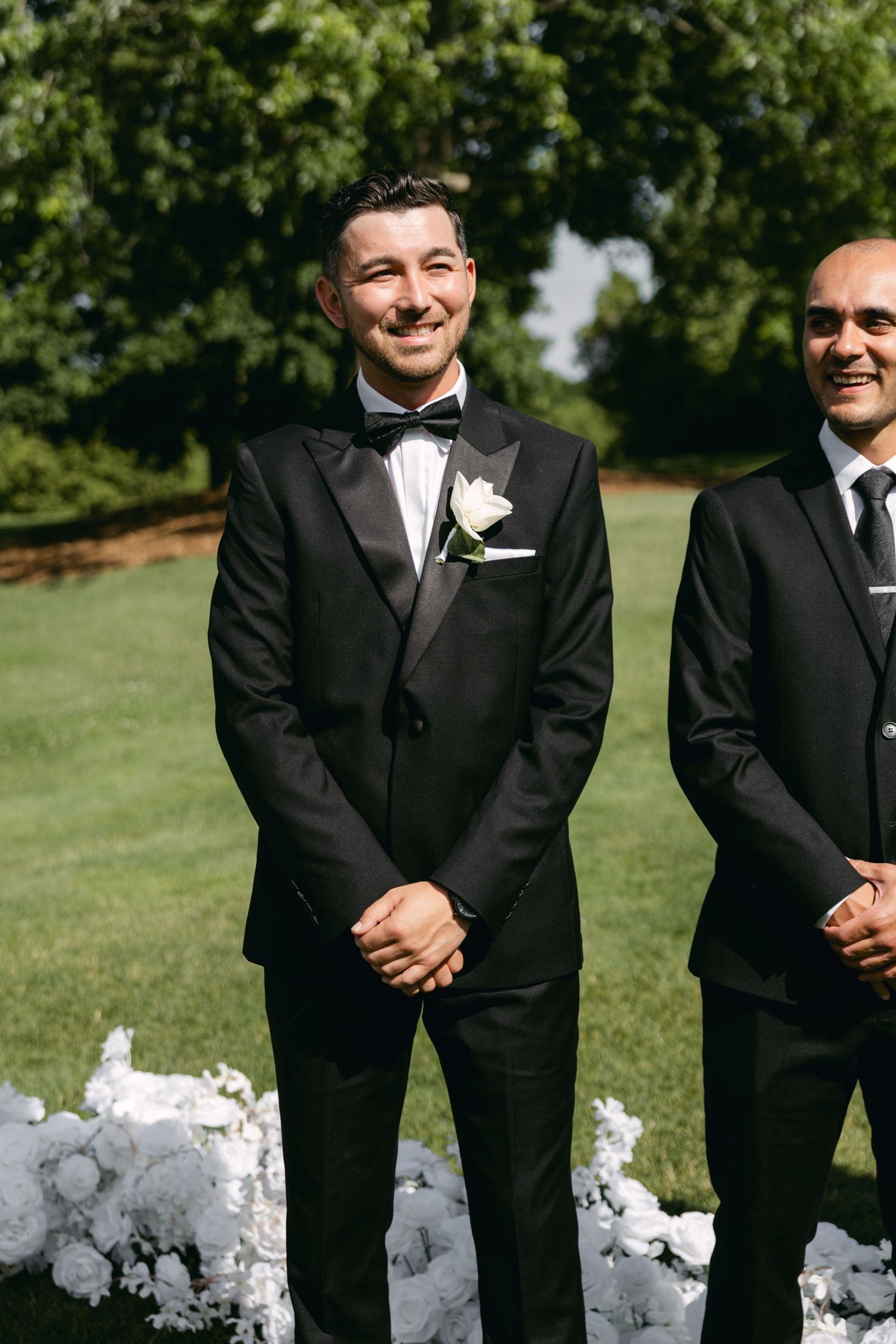Groomsmen in black tuxedos smile and pose together on a sunny golf course.