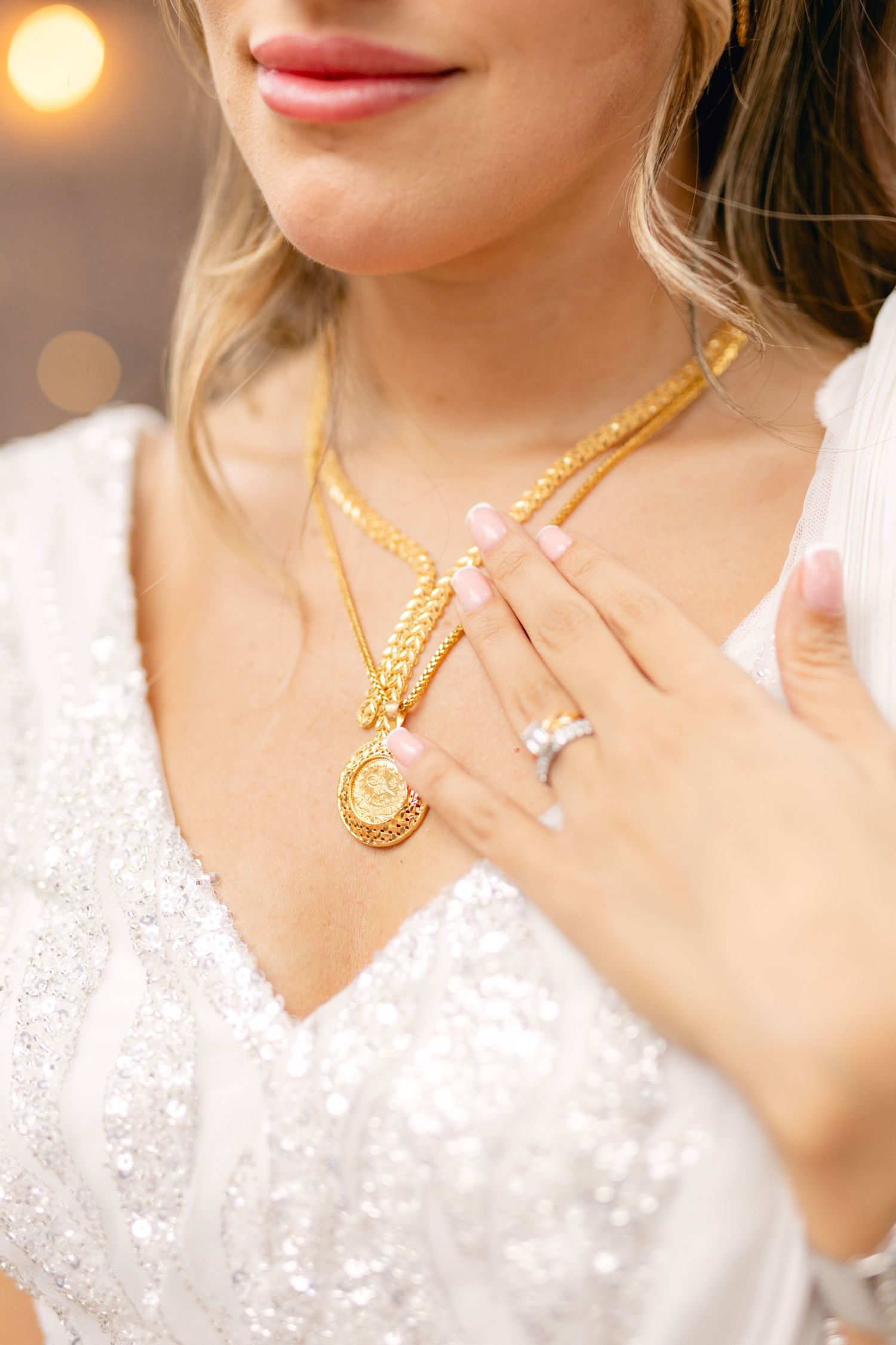 Close-up of bridal jewelry featuring gold necklaces and engagement ring.